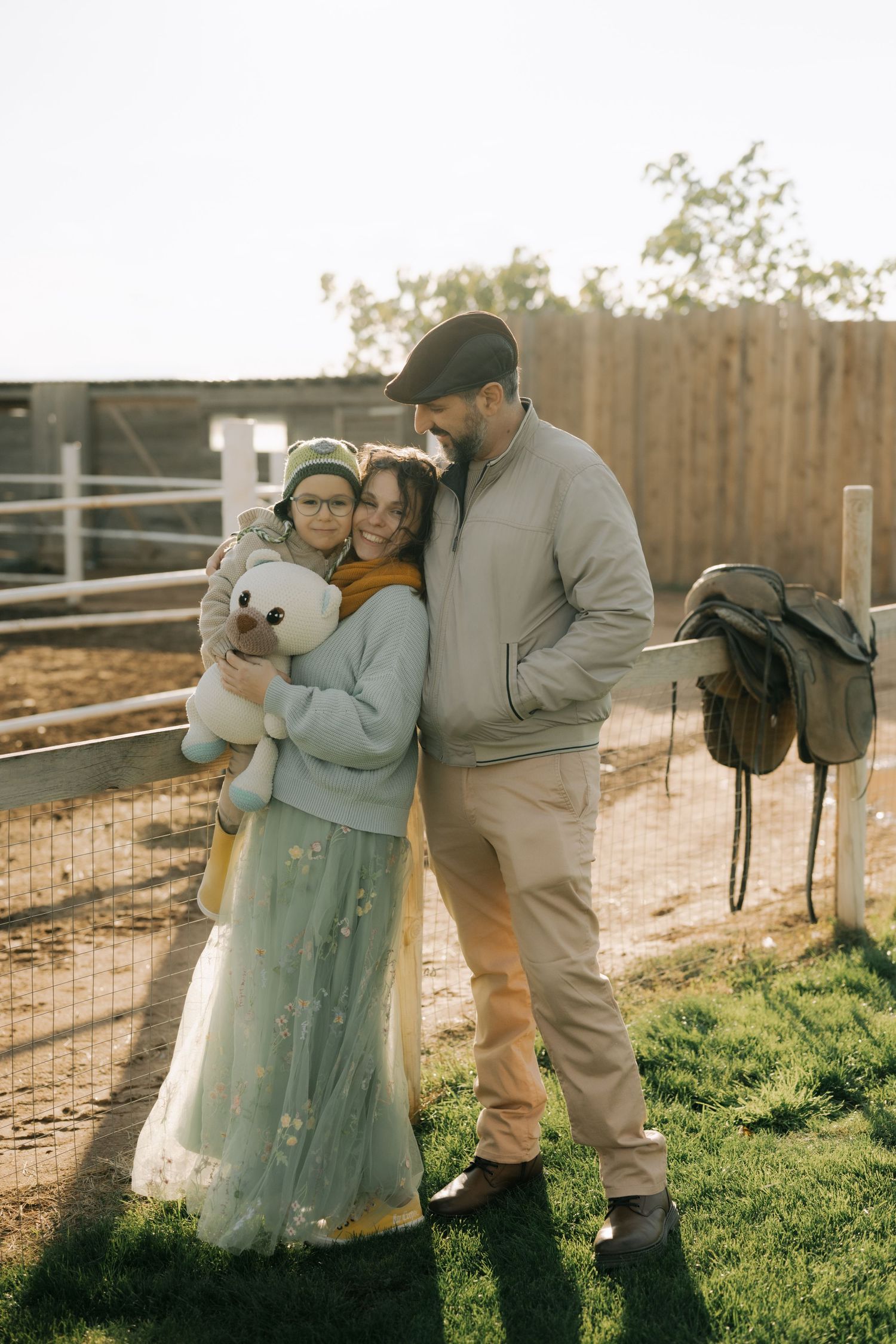 Multiple shots of a couple posing together with a white teddy bear in front of a wooden fence during golden hour.