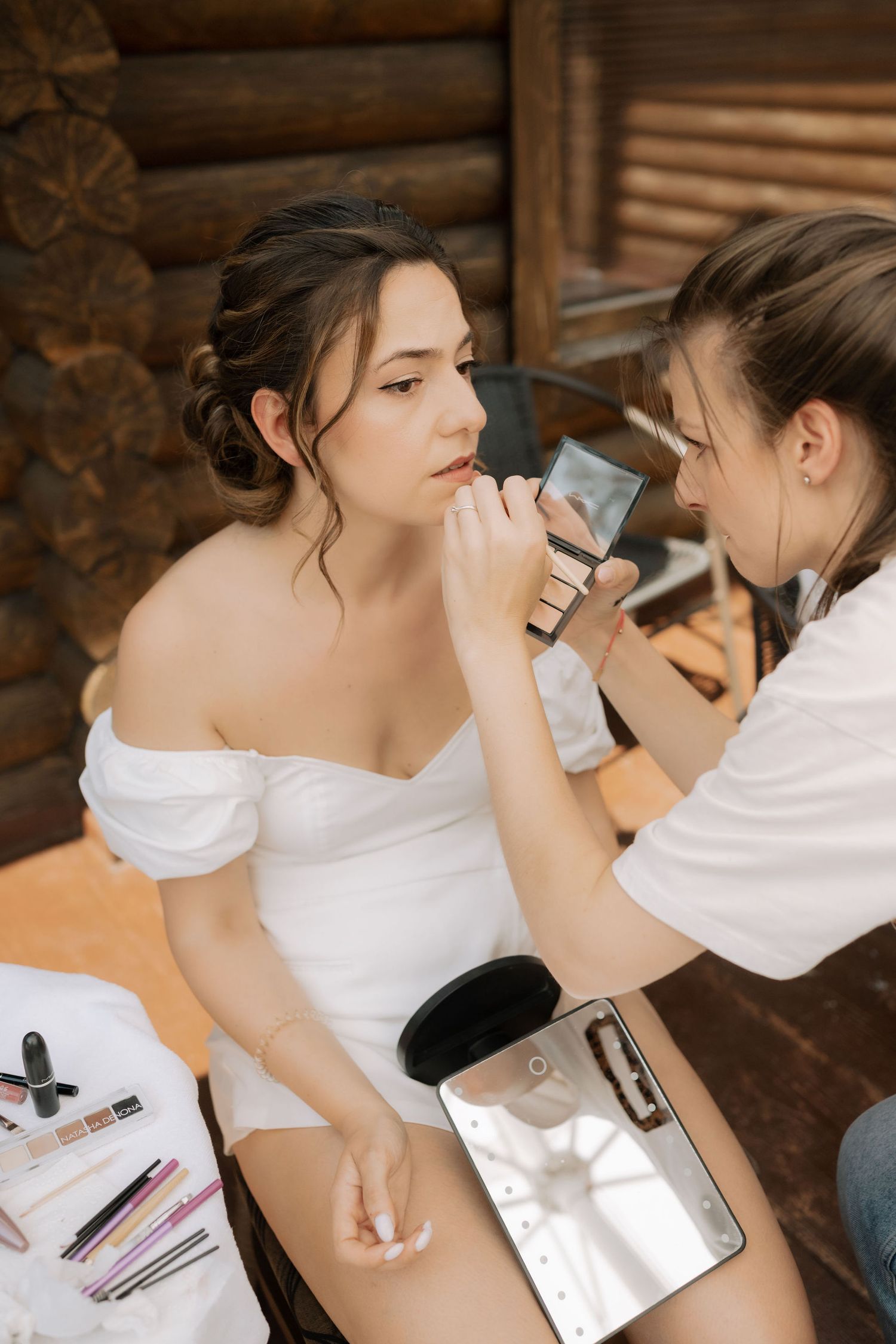 Professional makeup artist applying cosmetics on a person wearing a white dress.