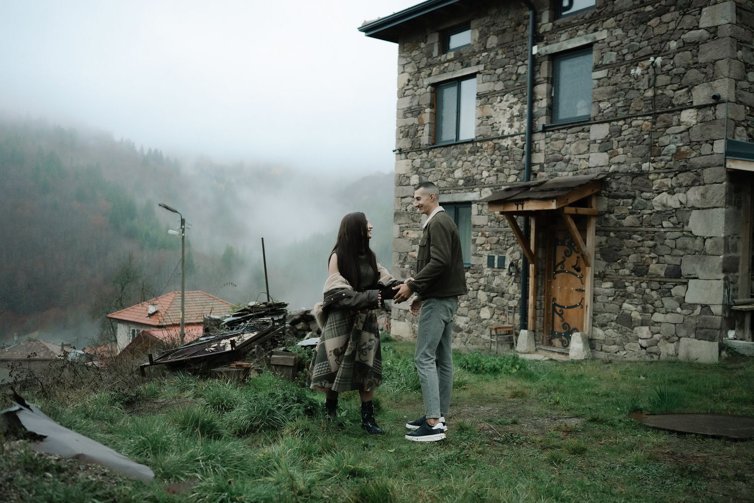 Stone buildings nestled in misty mountains create a moody atmospheric scene in rural countryside.
