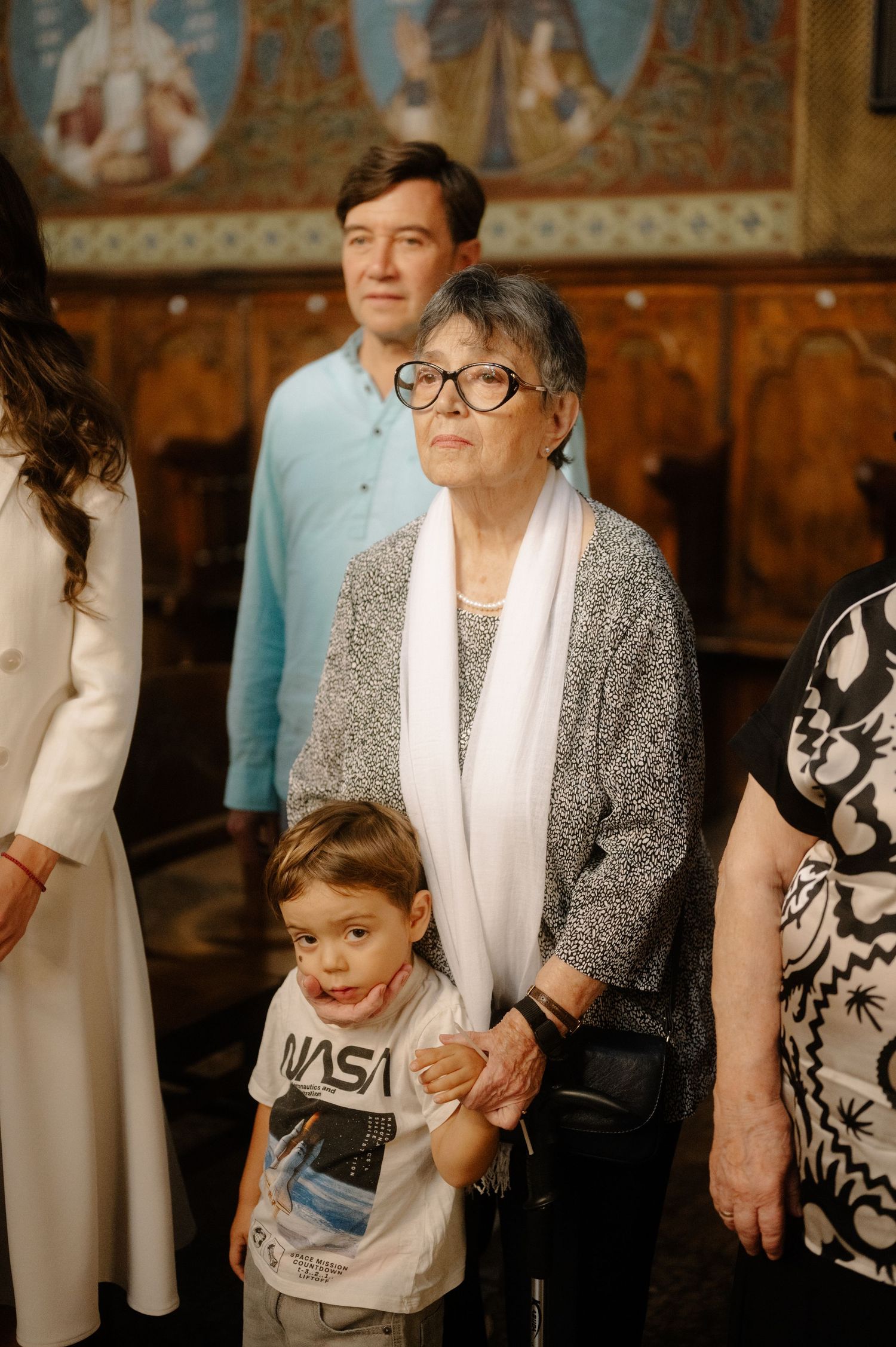 A child in a NASA t-shirt stands next to an elderly person wearing glasses and a white and gray outfit.