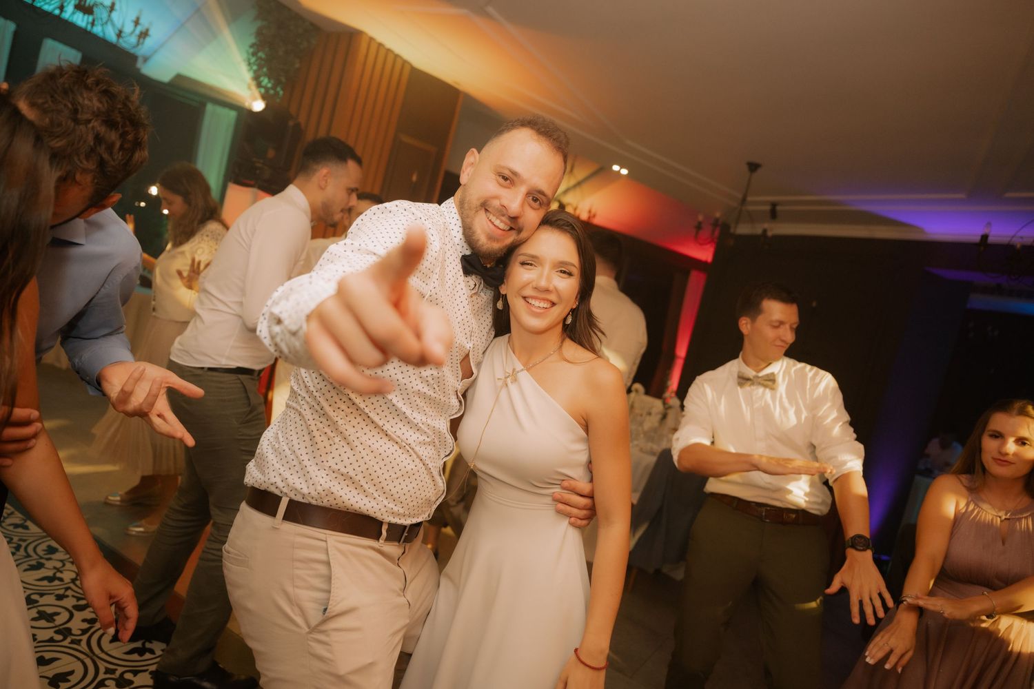 People dancing and celebrating together at a wedding reception with colorful lighting and festive atmosphere.
