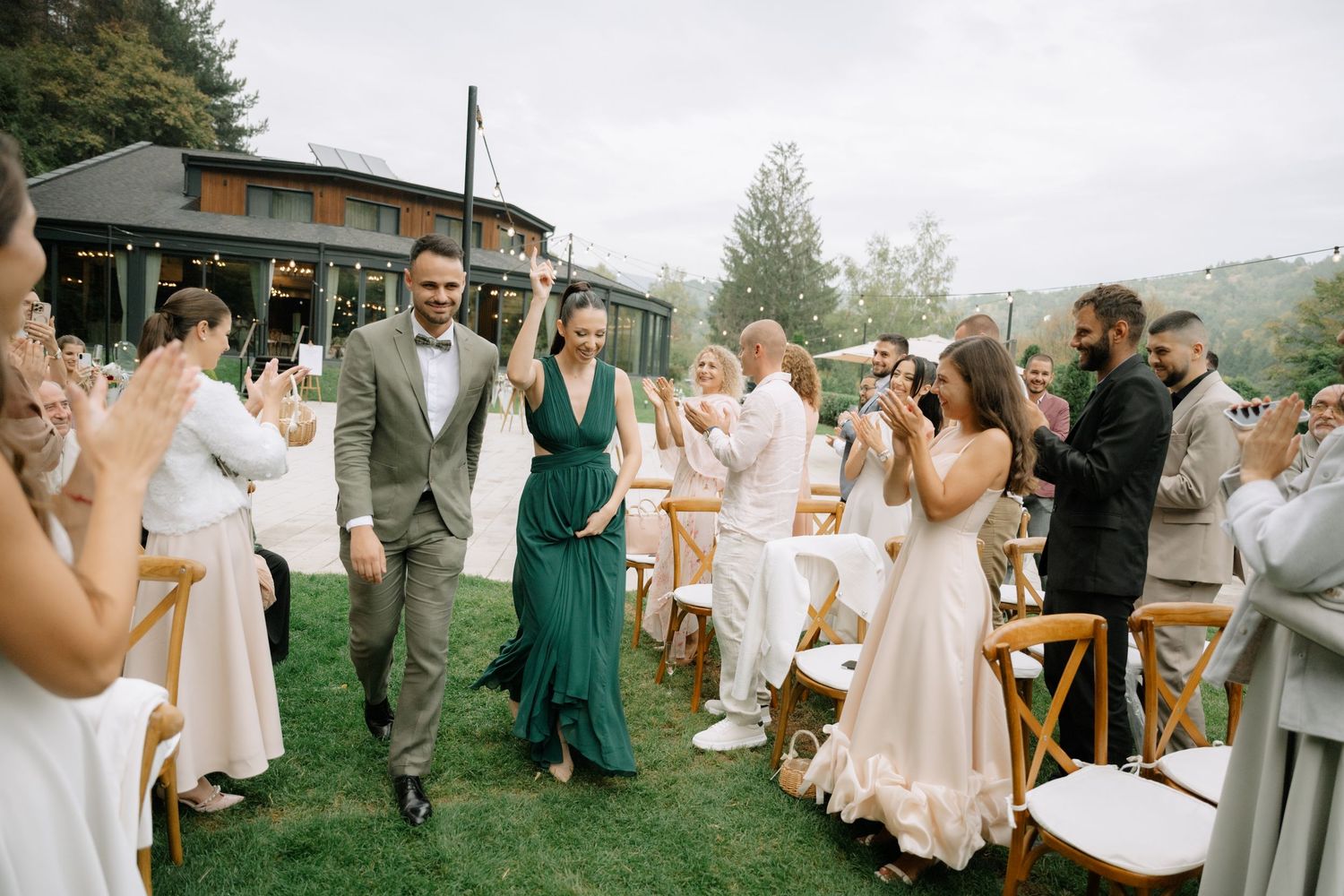 Wedding guests celebrate during an outdoor reception with people dressed in white and emerald green attire.