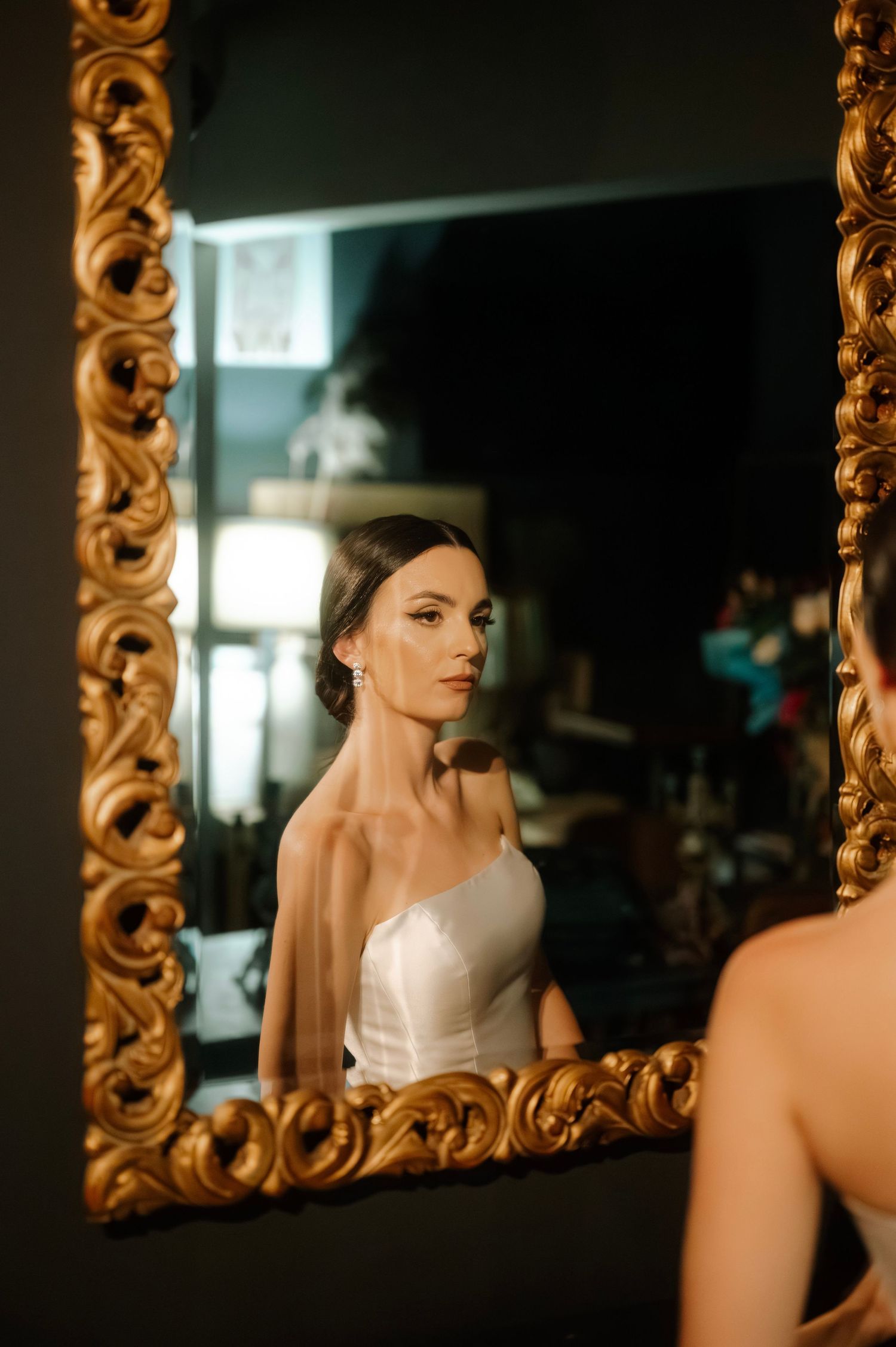 A series of reflections in an ornate gold mirror shows a figure in a white dress against a dark background.