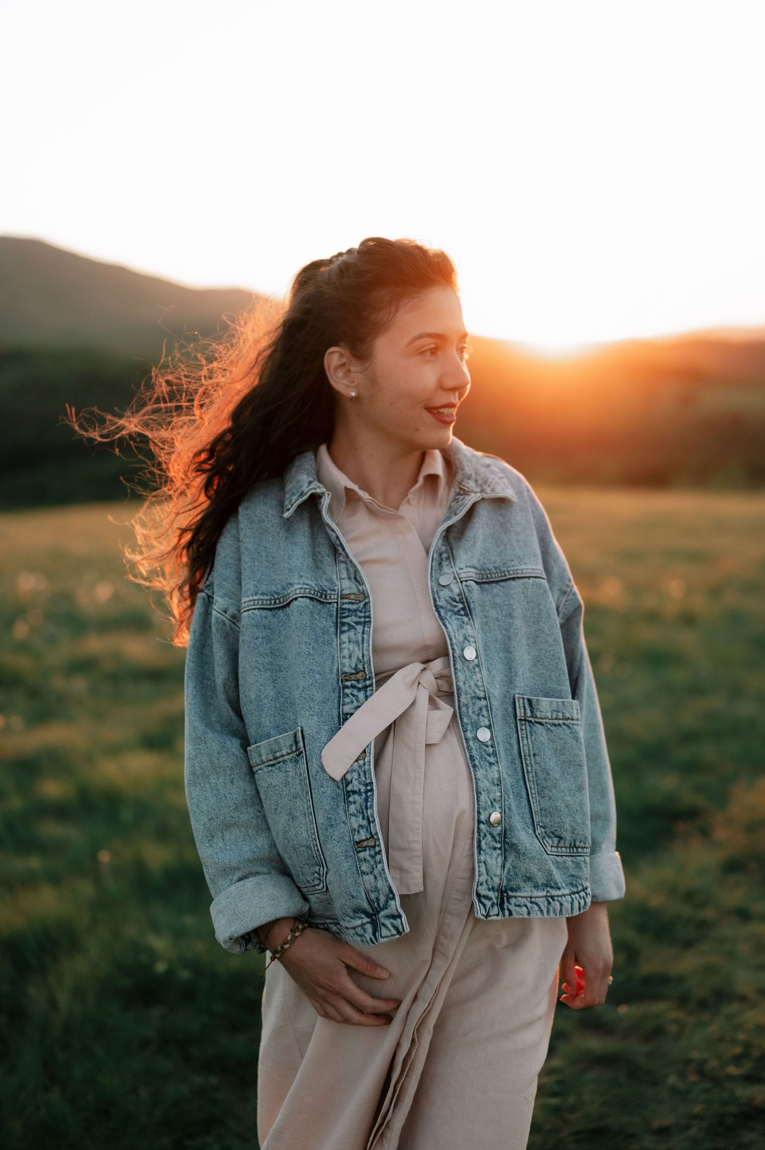 A person in a denim jacket laughs joyfully while standing in a golden field at sunset.