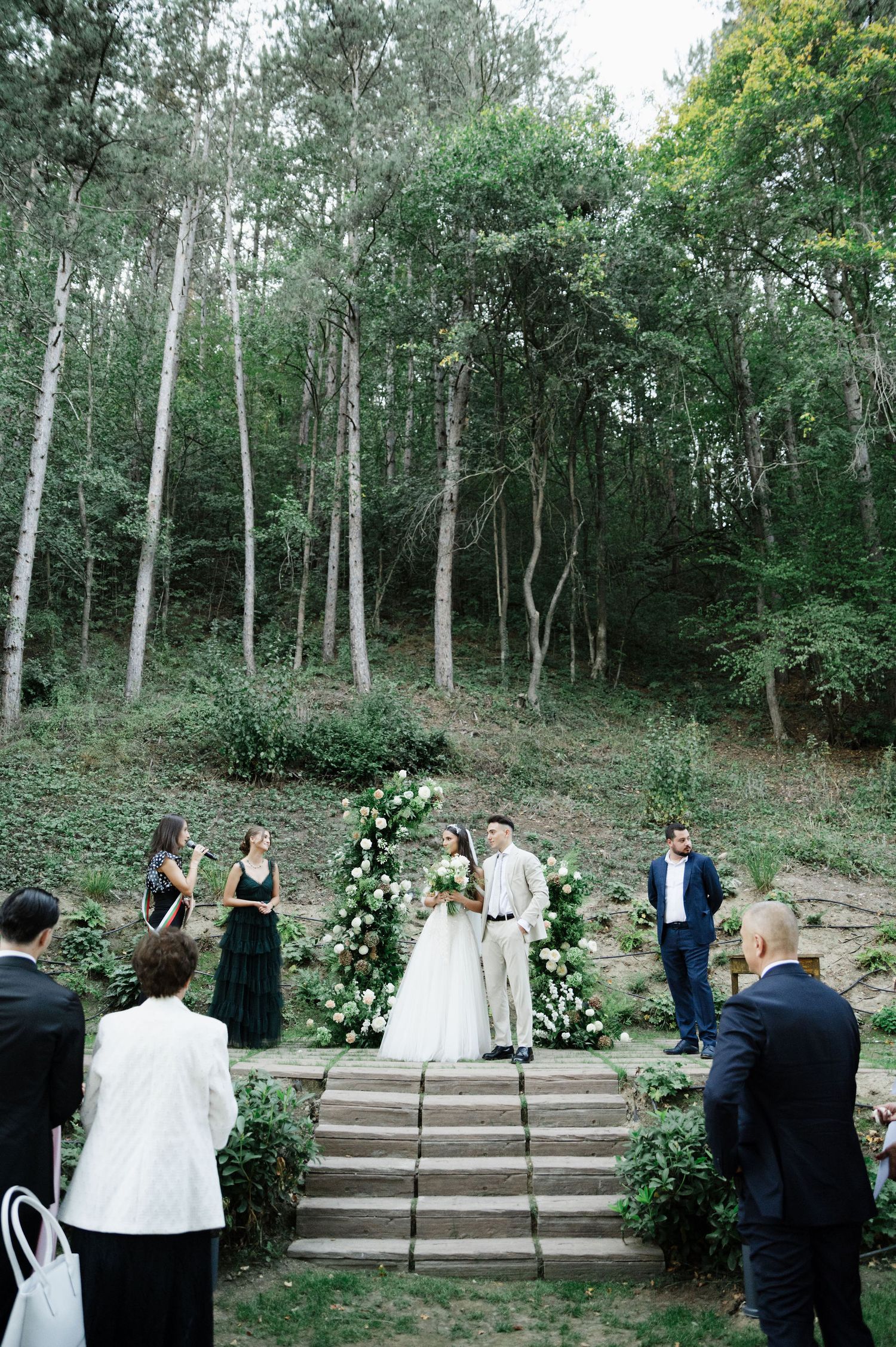Wedding photographers capturing ceremony moments on woodland stone steps with floral decor.