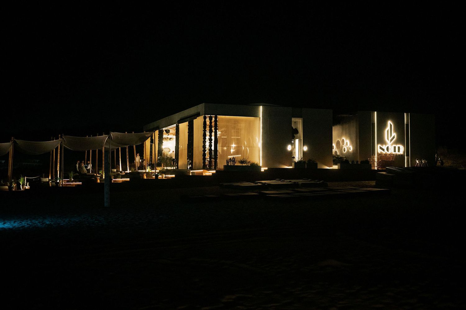 Dark outdoor nighttime venue illuminated by string lights and distant building silhouettes.