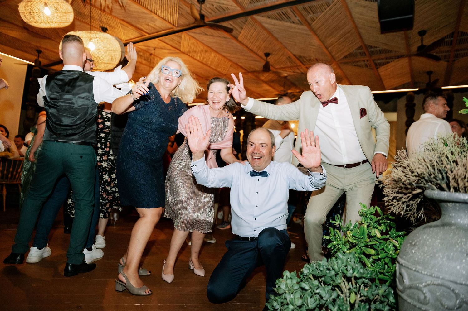 Wedding guests dancing together on a wooden floor under decorative pendant lights.