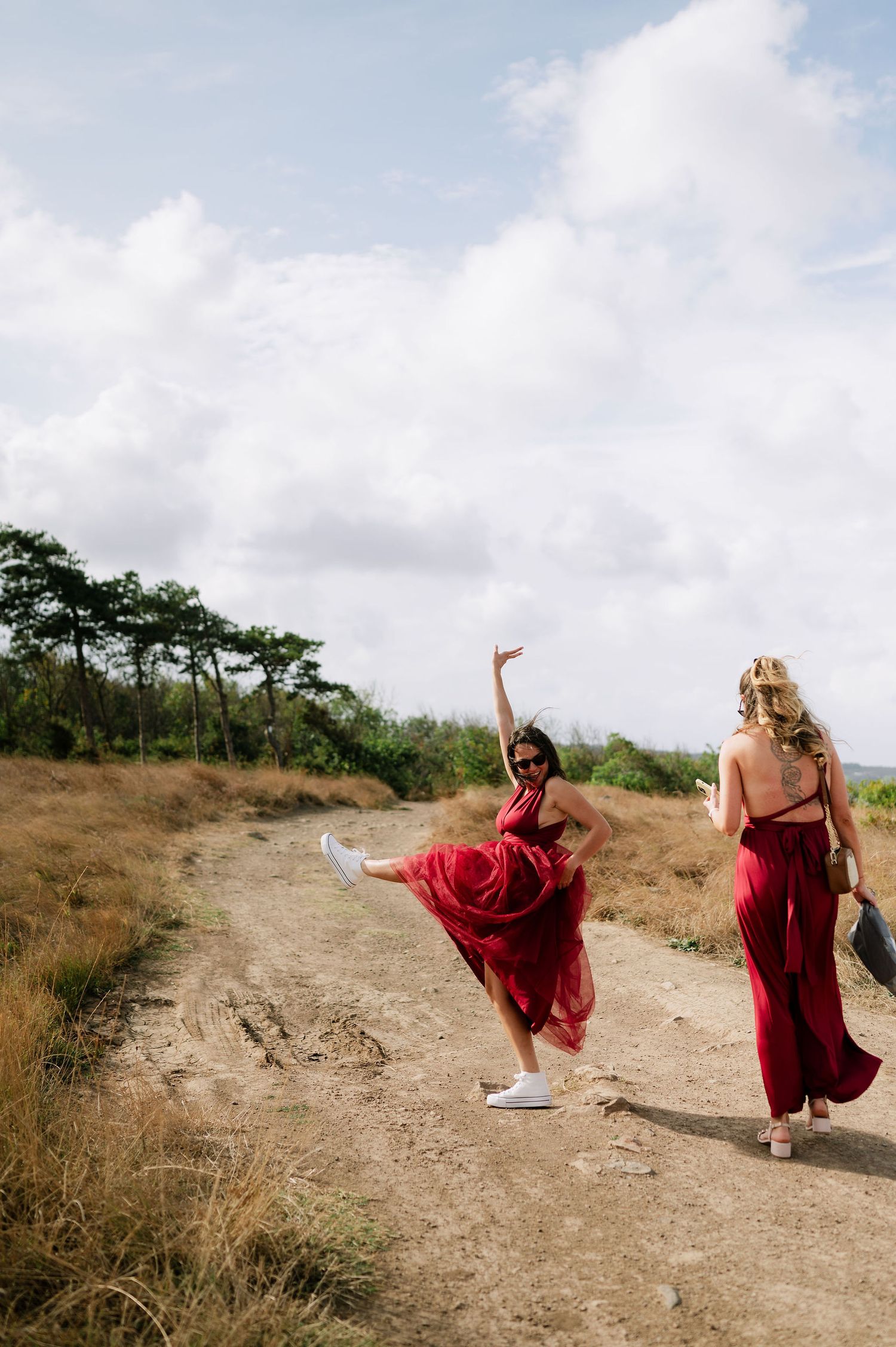 Women in flowing red dresses run and dance along a hilltop path.
