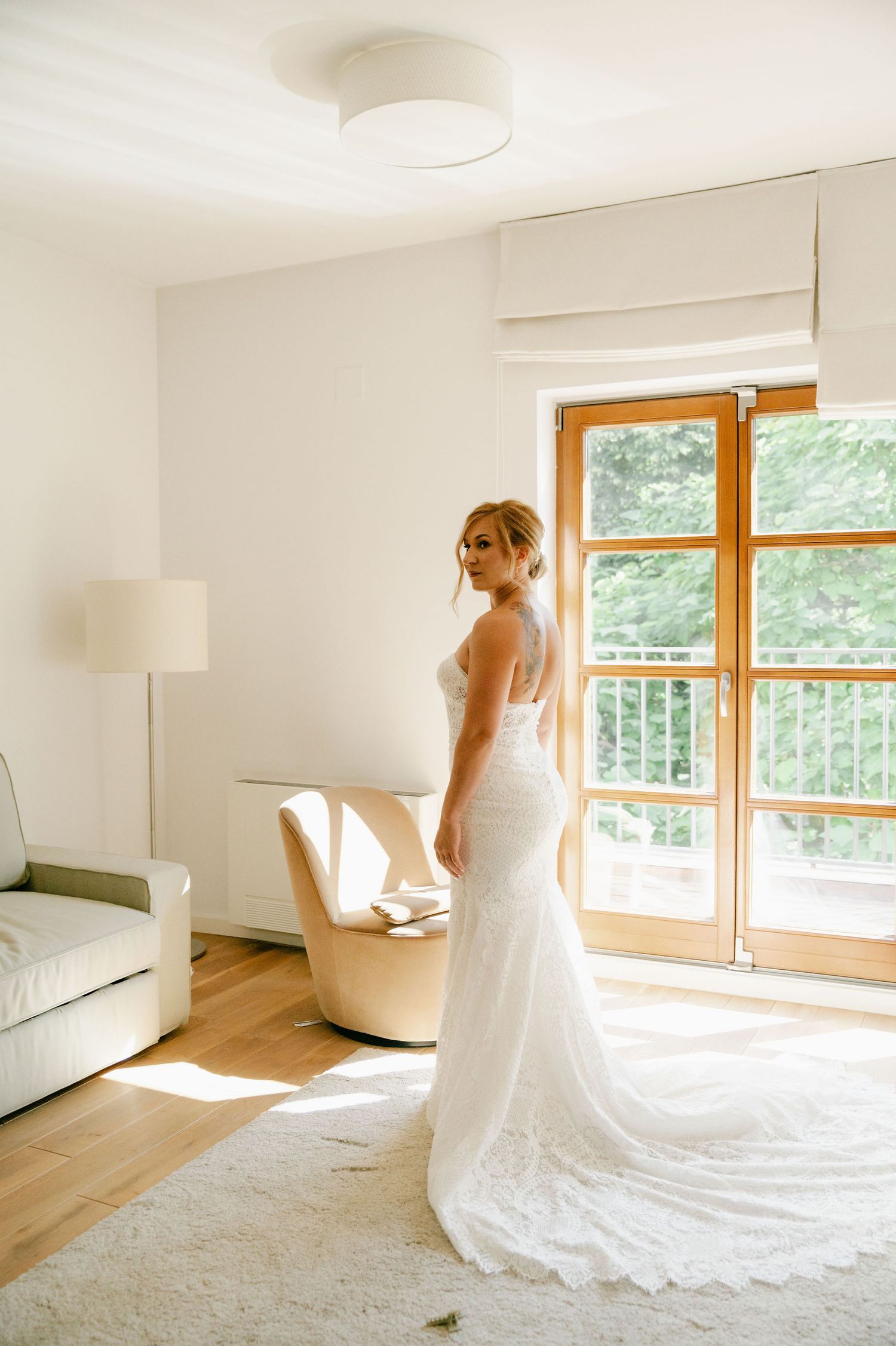 An elegant wedding dress with lace train photographed in a bright modern room with hardwood floors.