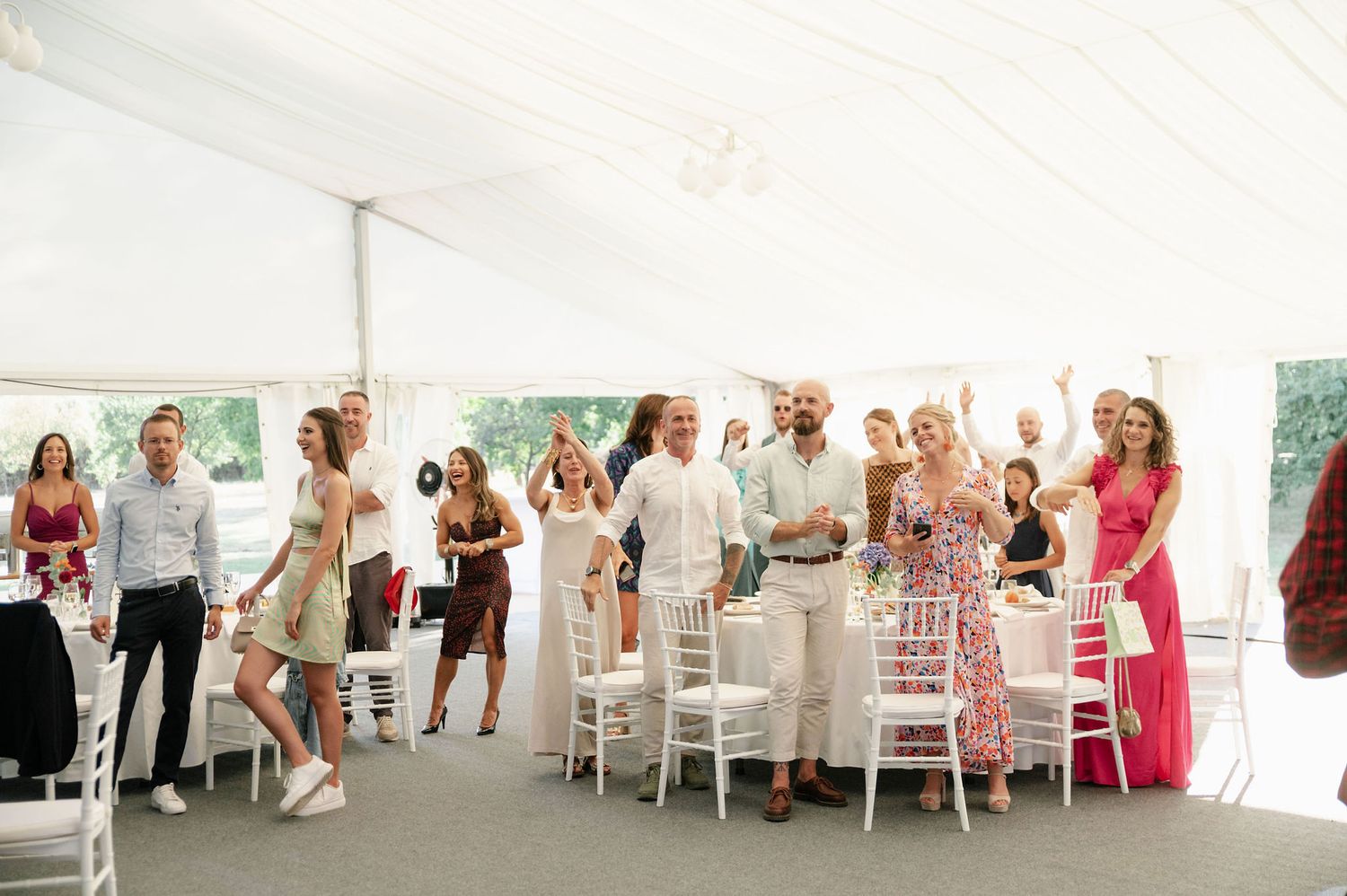 Wedding reception guests seated at elegant white tables in a bright tent venue.
