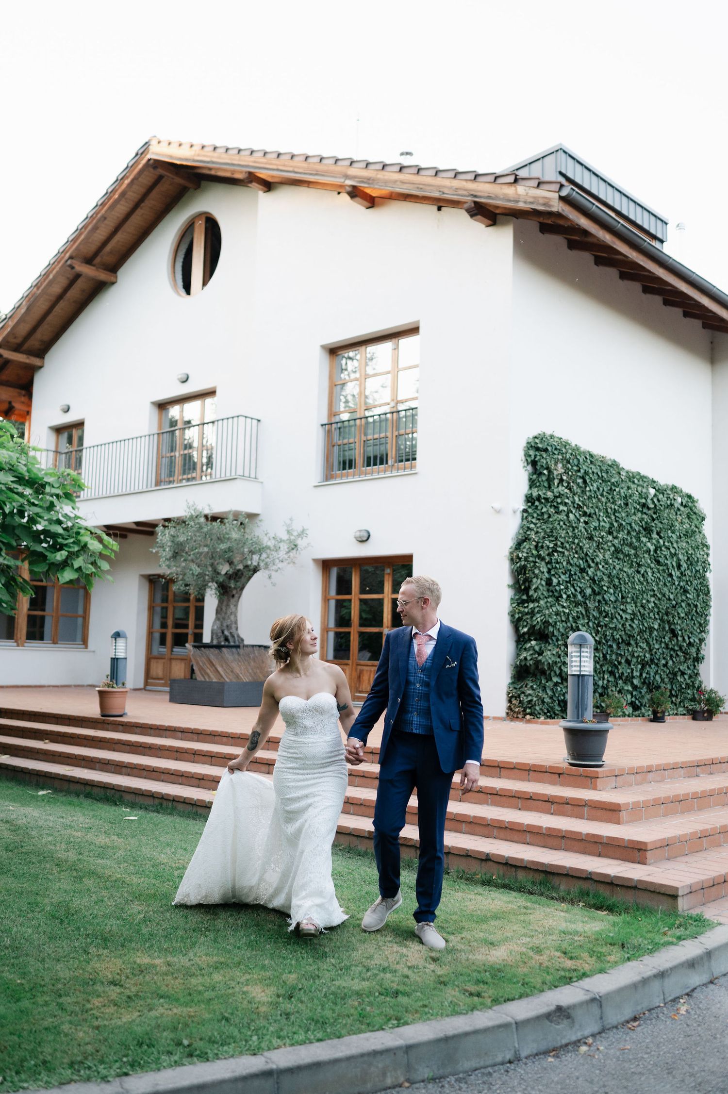 A bride in white dress and groom in navy suit dance together on a manicured lawn.