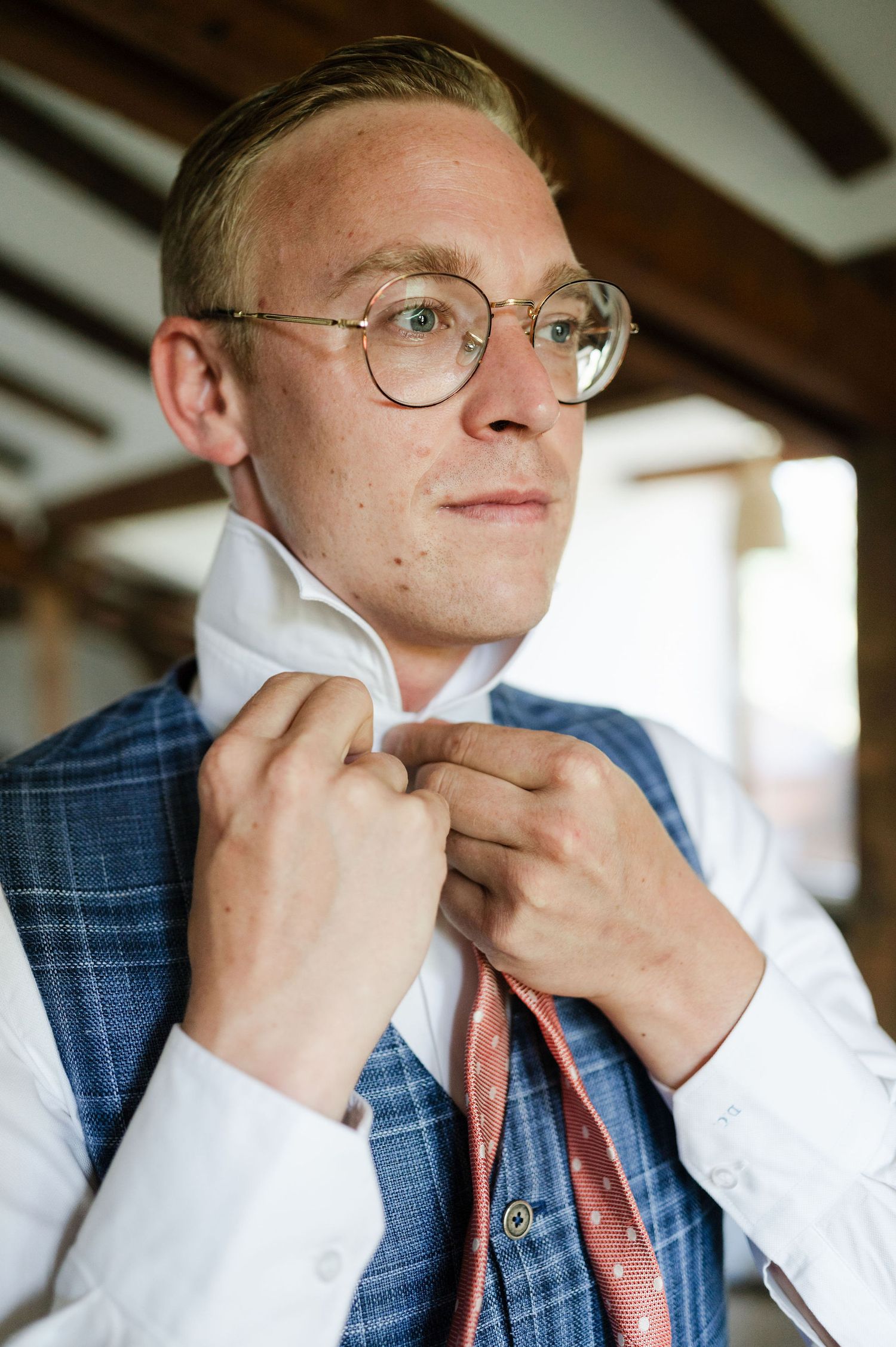 Person adjusting a white dress shirt collar while wearing a blue vest and coral tie.