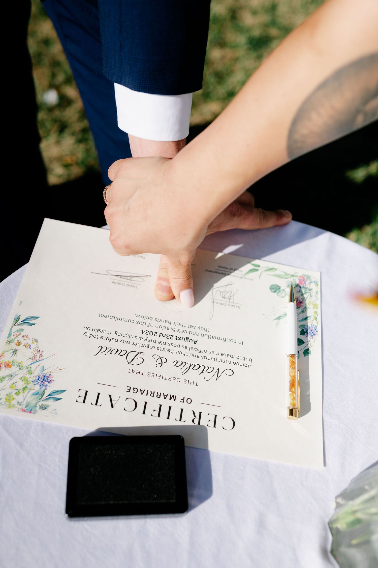 Close-up of hands signing wedding certificate with floral decorated papers.