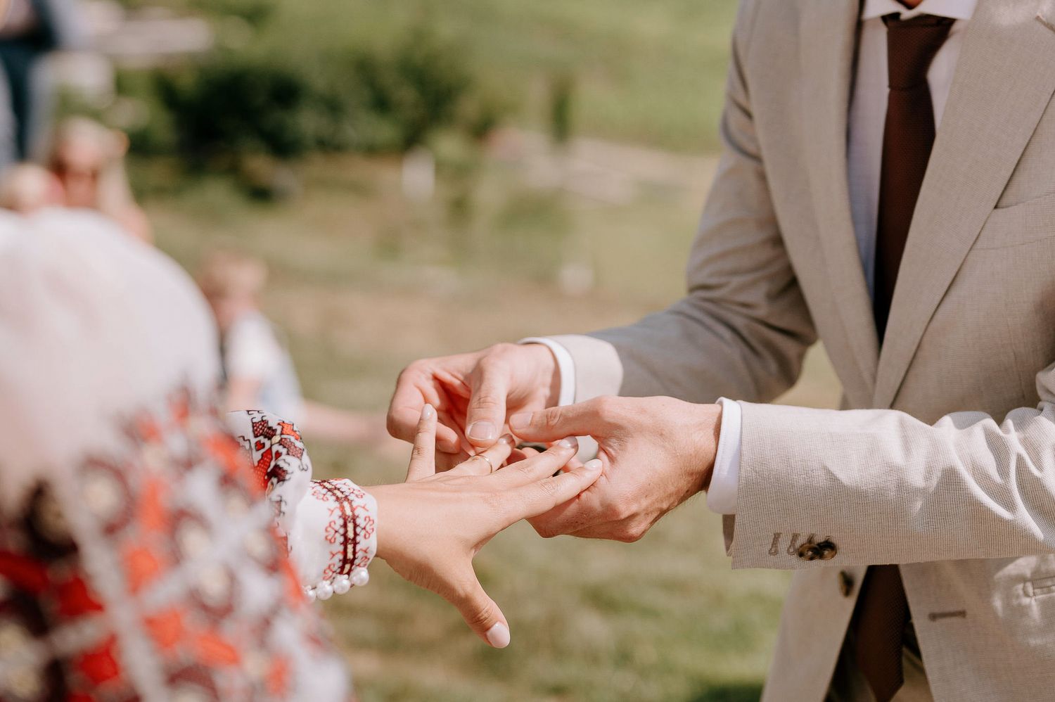 Close-up of hands exchanging rings during an outdoor wedding ceremony.
