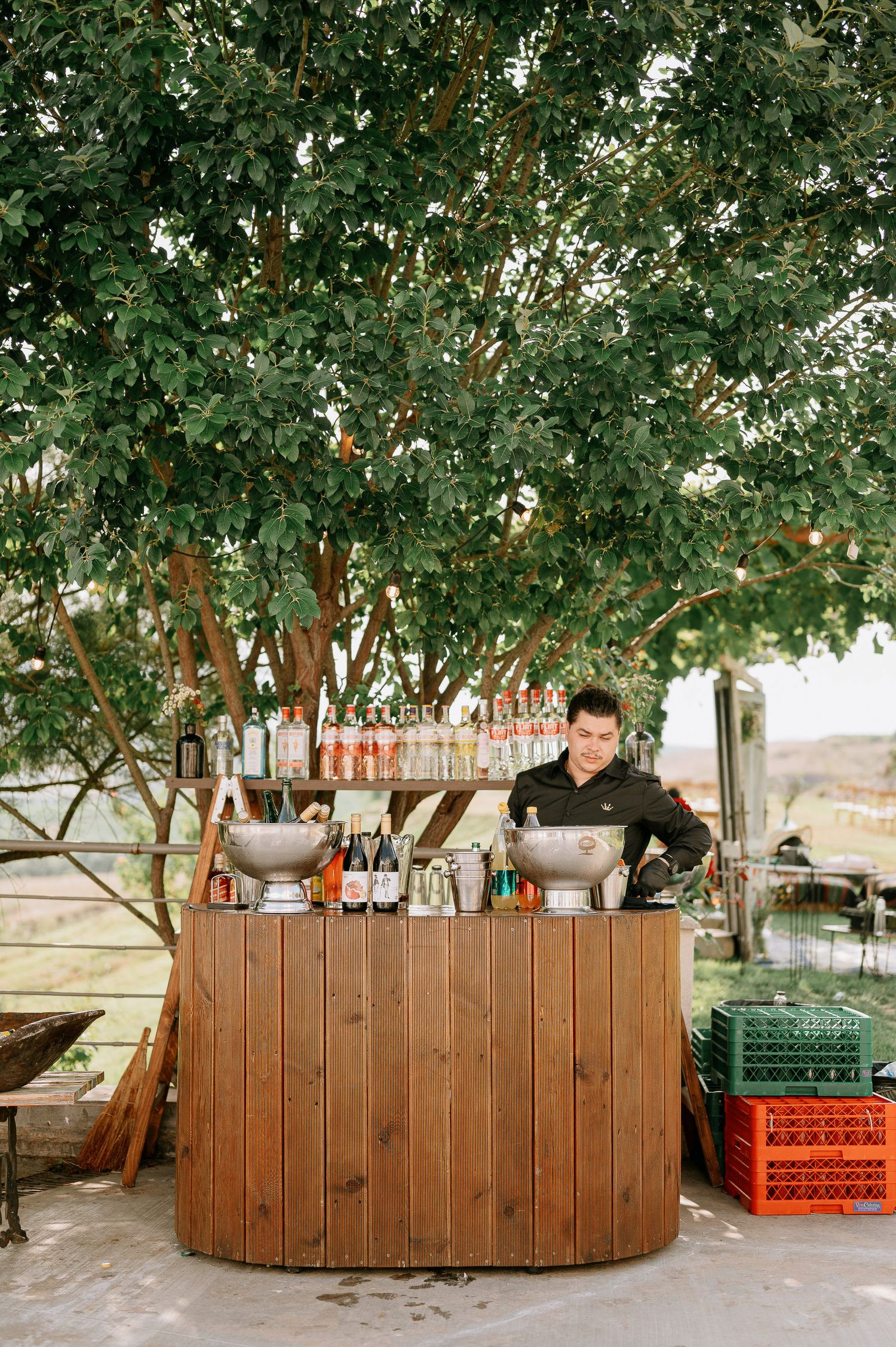 Wooden bar setup under green trees at an outdoor wedding venue.