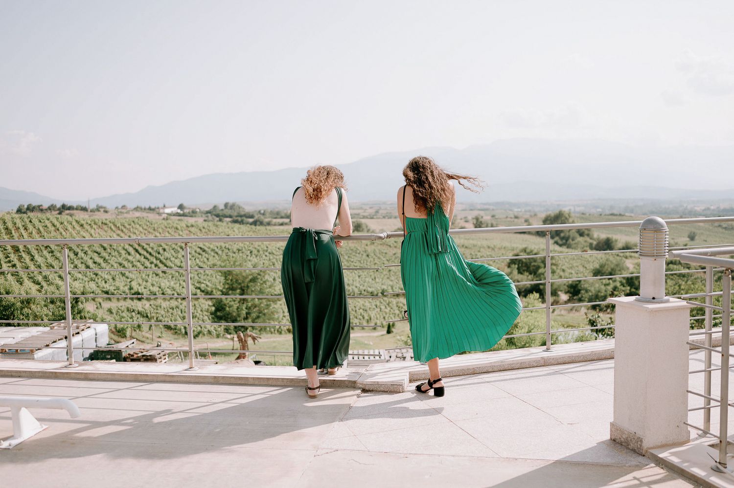 People standing on a white terrace overlooking a scenic vineyard landscape.