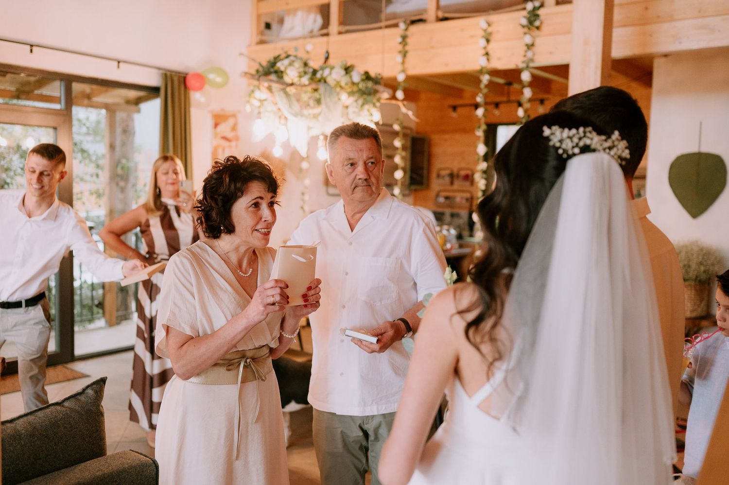 Guests celebrate at an intimate indoor wedding reception decorated with string lights and floral arrangements.