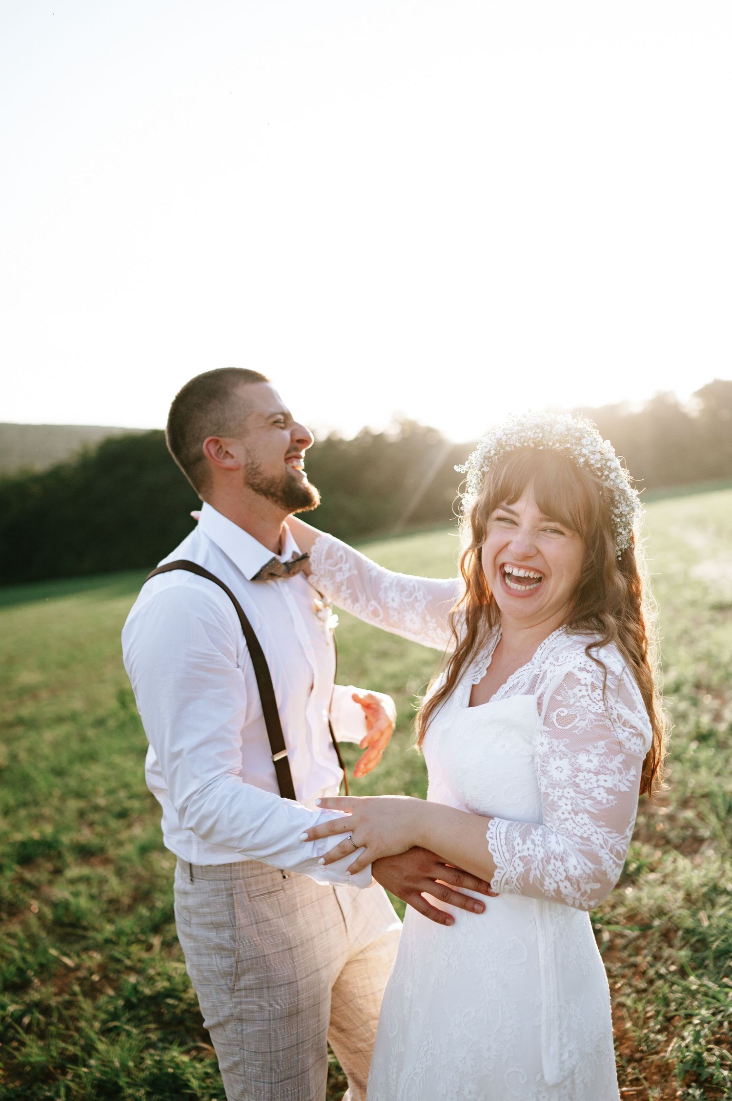 Newlywed couple laughs together in a sunlit field during golden hour photo session.