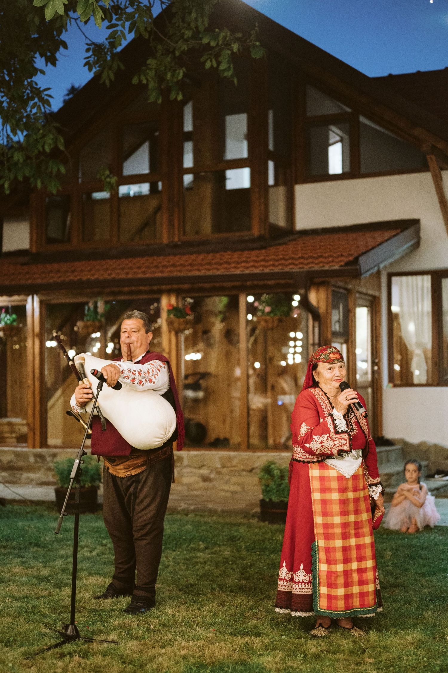 Traditional folk musicians in cultural dress performing at outdoor event near rustic building.