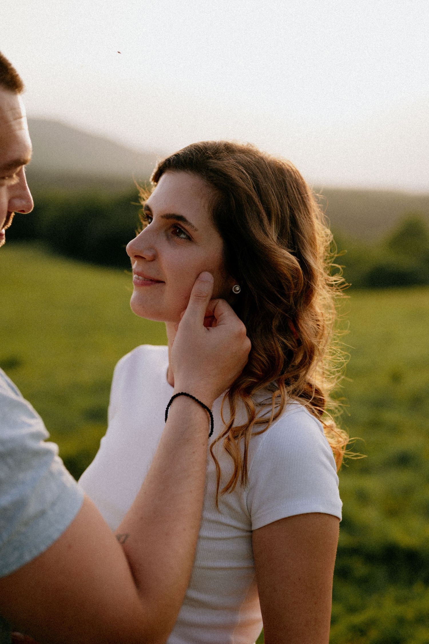 A gentle touch on the cheek during an intimate outdoor portrait session at sunset.