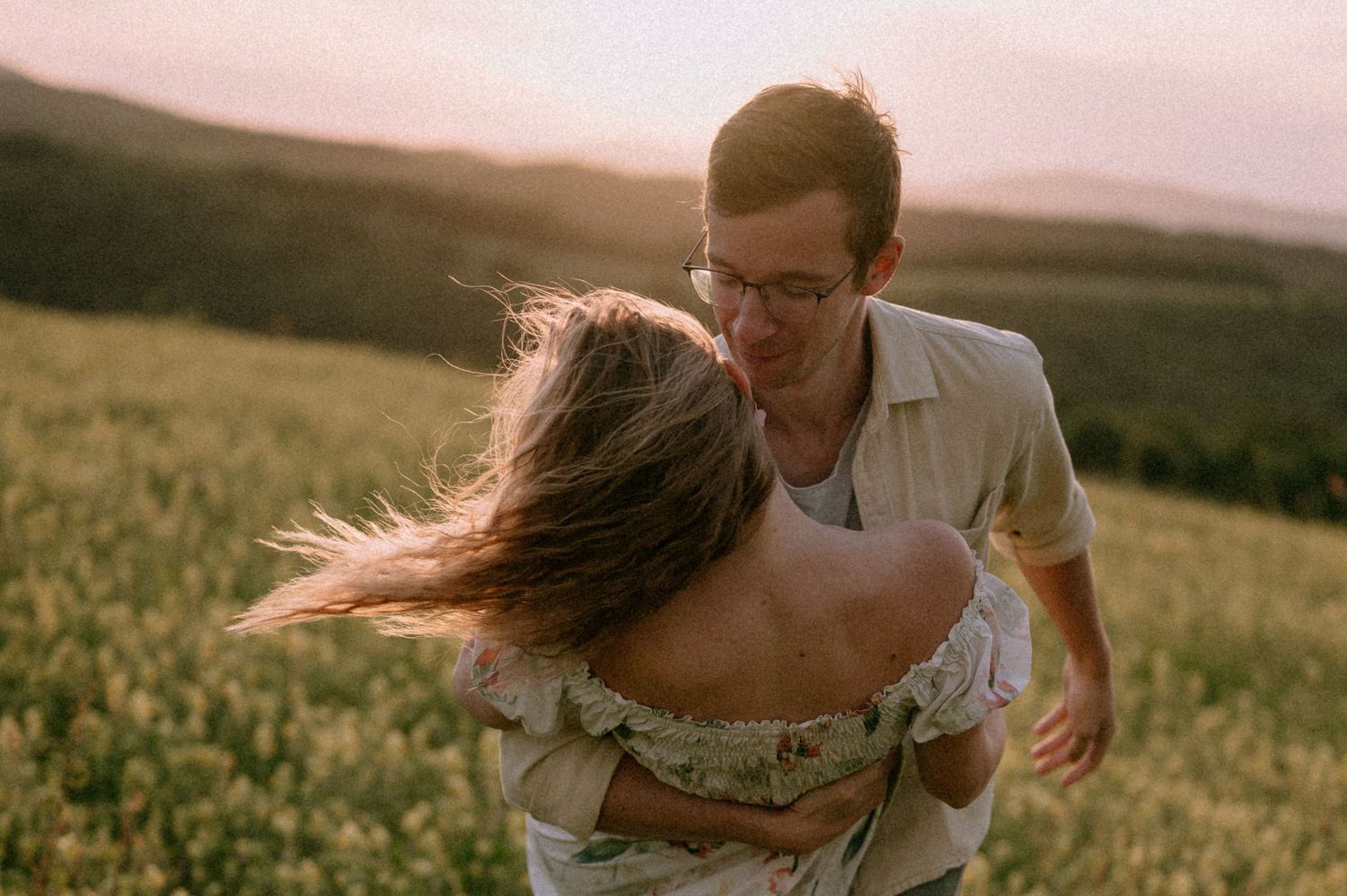A couple dances playfully in a golden field during sunset.