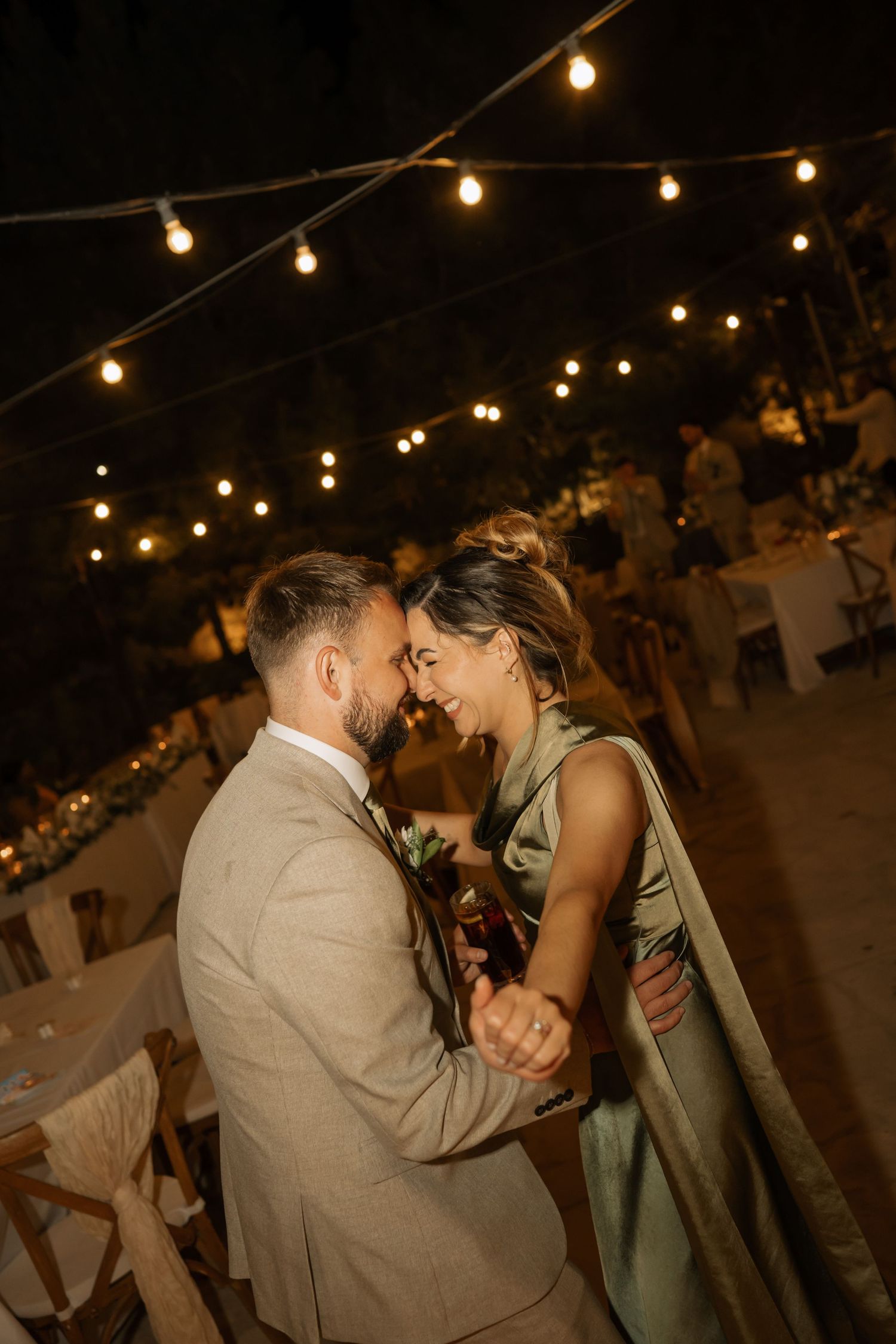 Couple sharing a romantic first dance under warm string lights at an outdoor evening wedding reception.