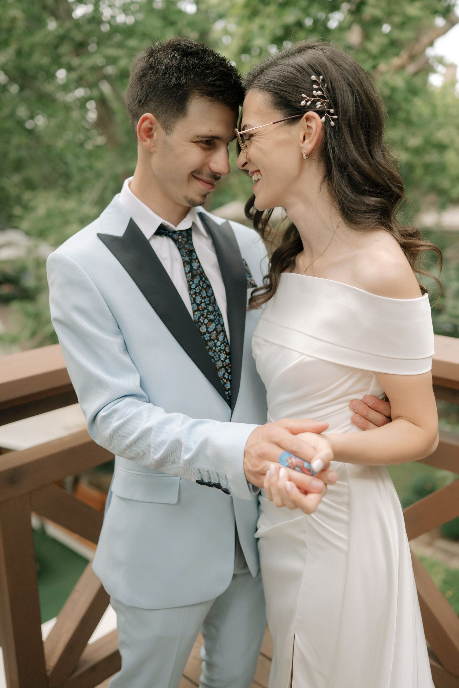A romantic wedding moment captured outdoors showing a couple in elegant attire sharing an intimate laugh together.