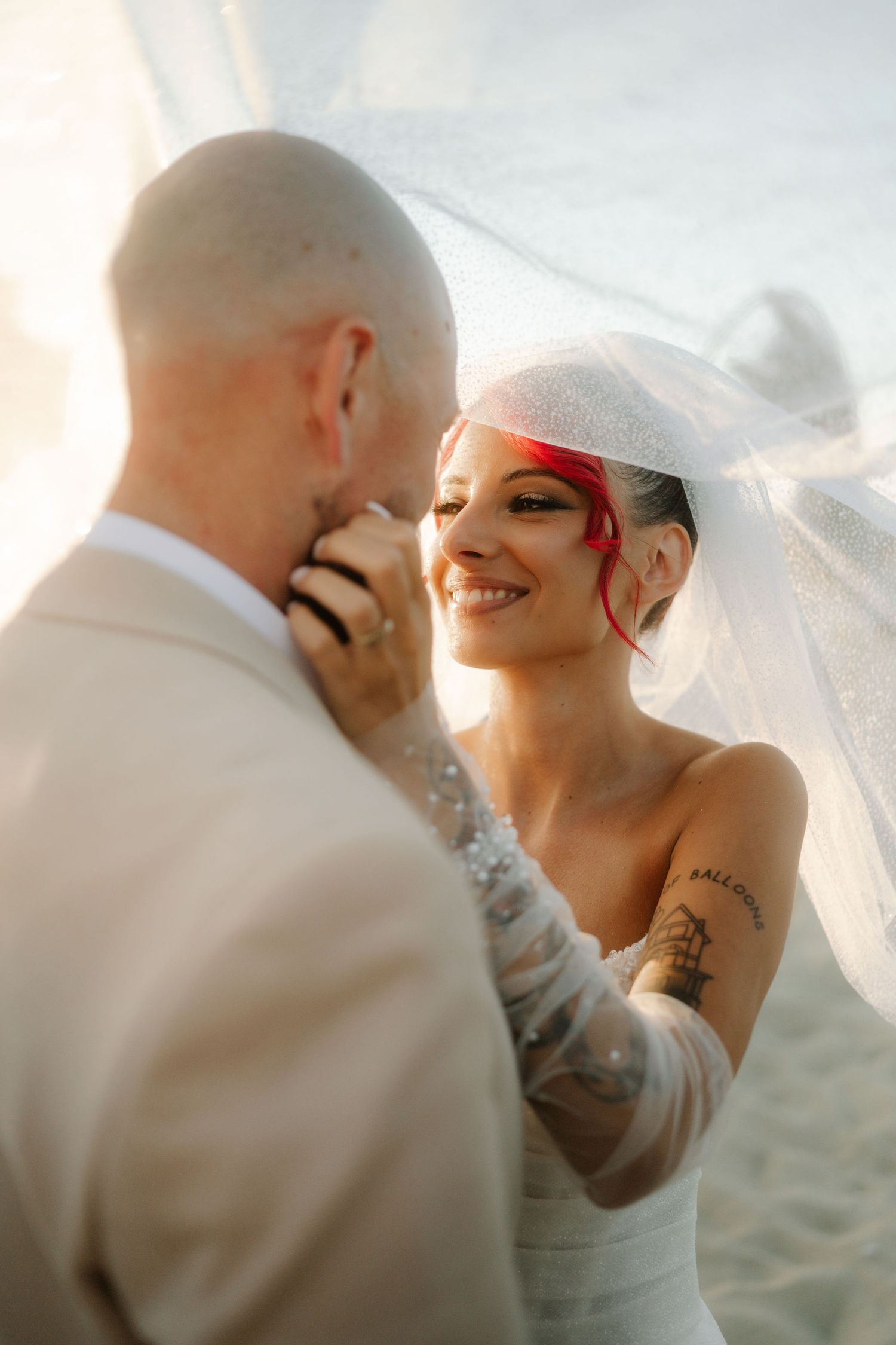 A romantic moment between newlyweds under a flowing veil during sunset.