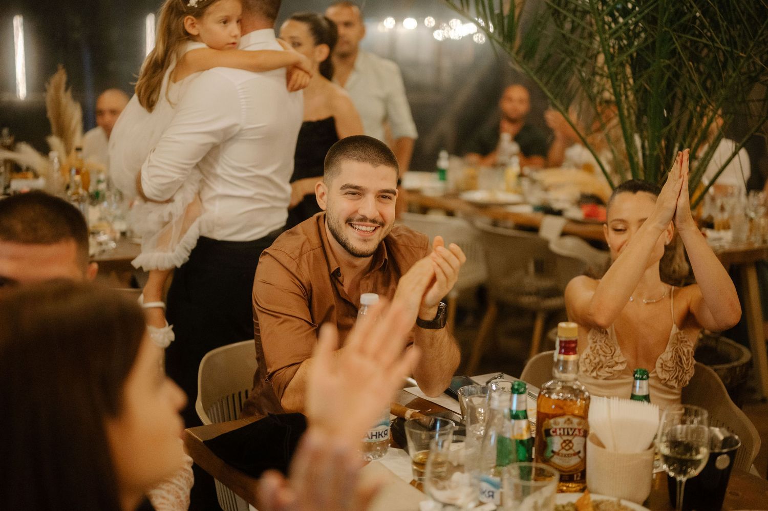 People enjoying dinner and drinks at a warmly lit outdoor restaurant patio during evening hours.