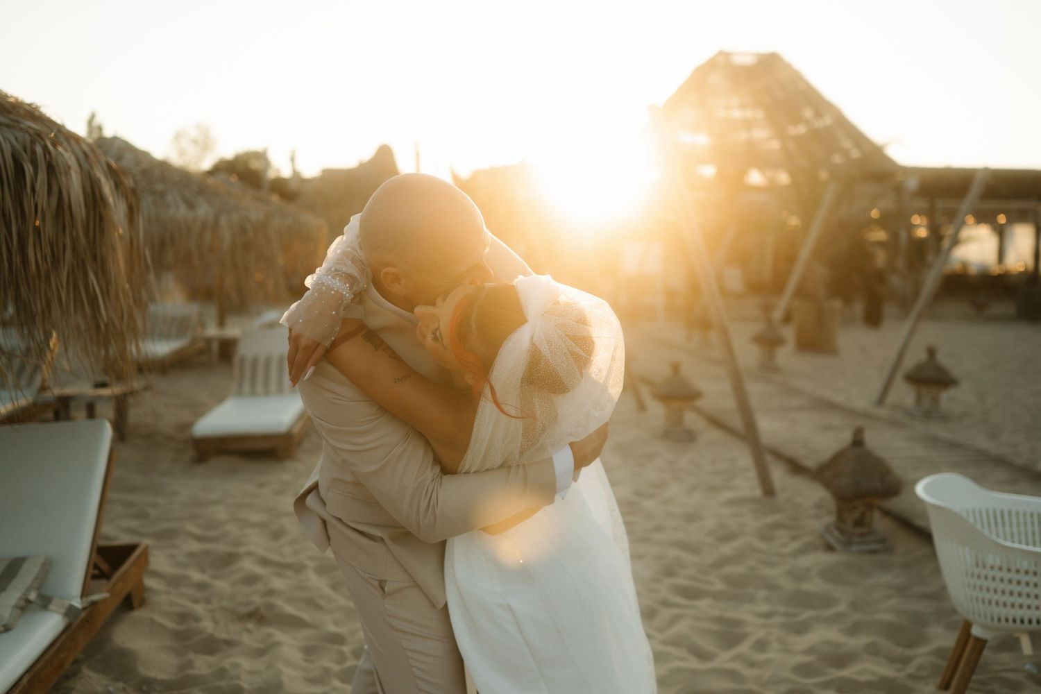 Romantic couple embraces on sandy beach during golden sunset with picnic basket and blanket.