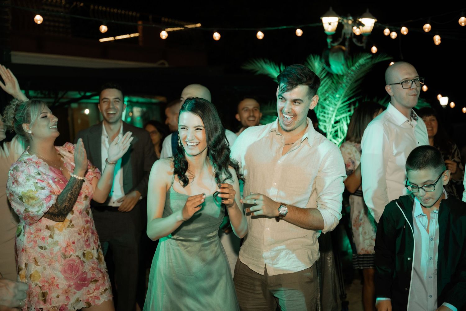 People dancing and celebrating at a lively party with green lighting and festive atmosphere.