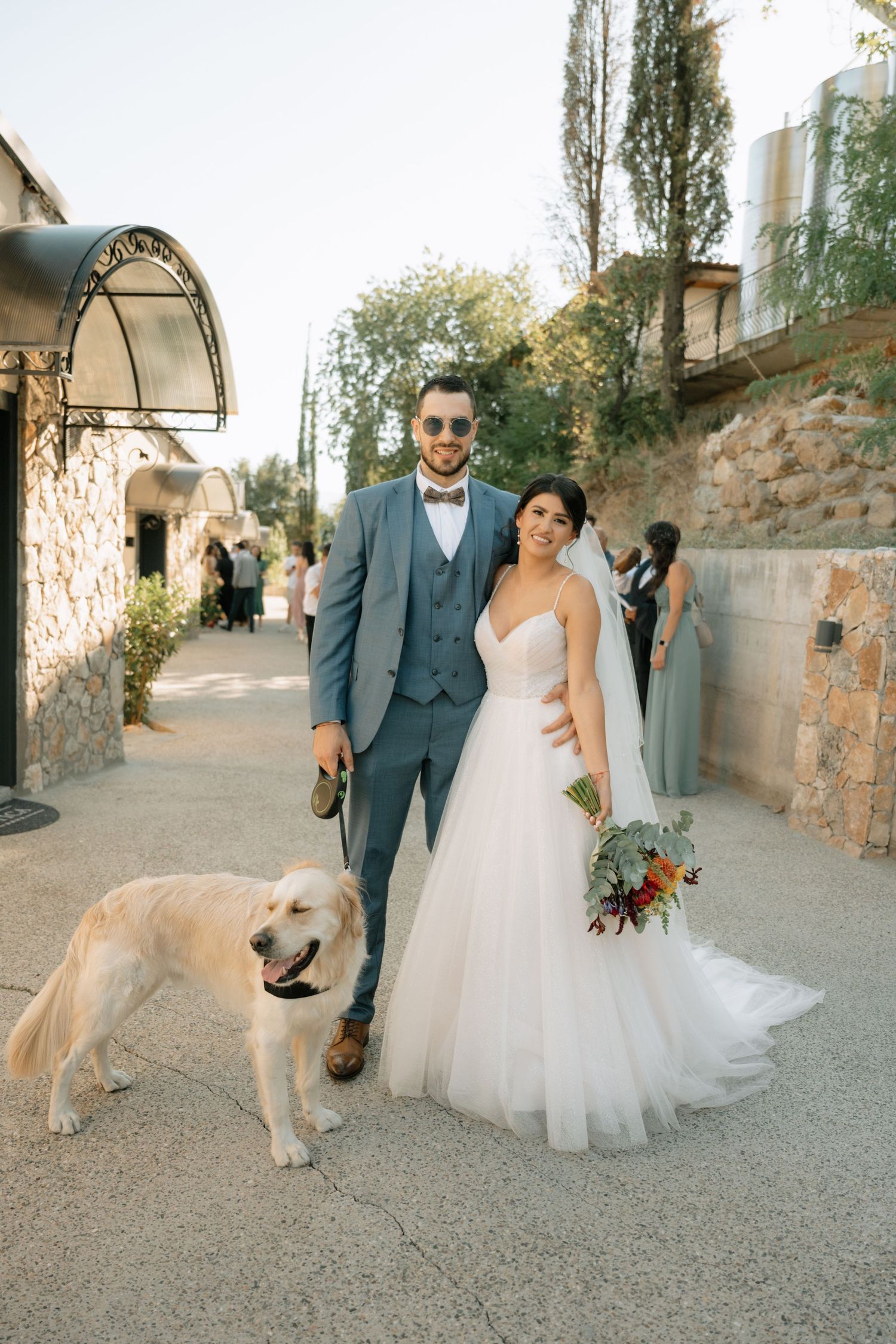 A couple in wedding attire poses with their golden retriever on a rustic stone path during their special day.