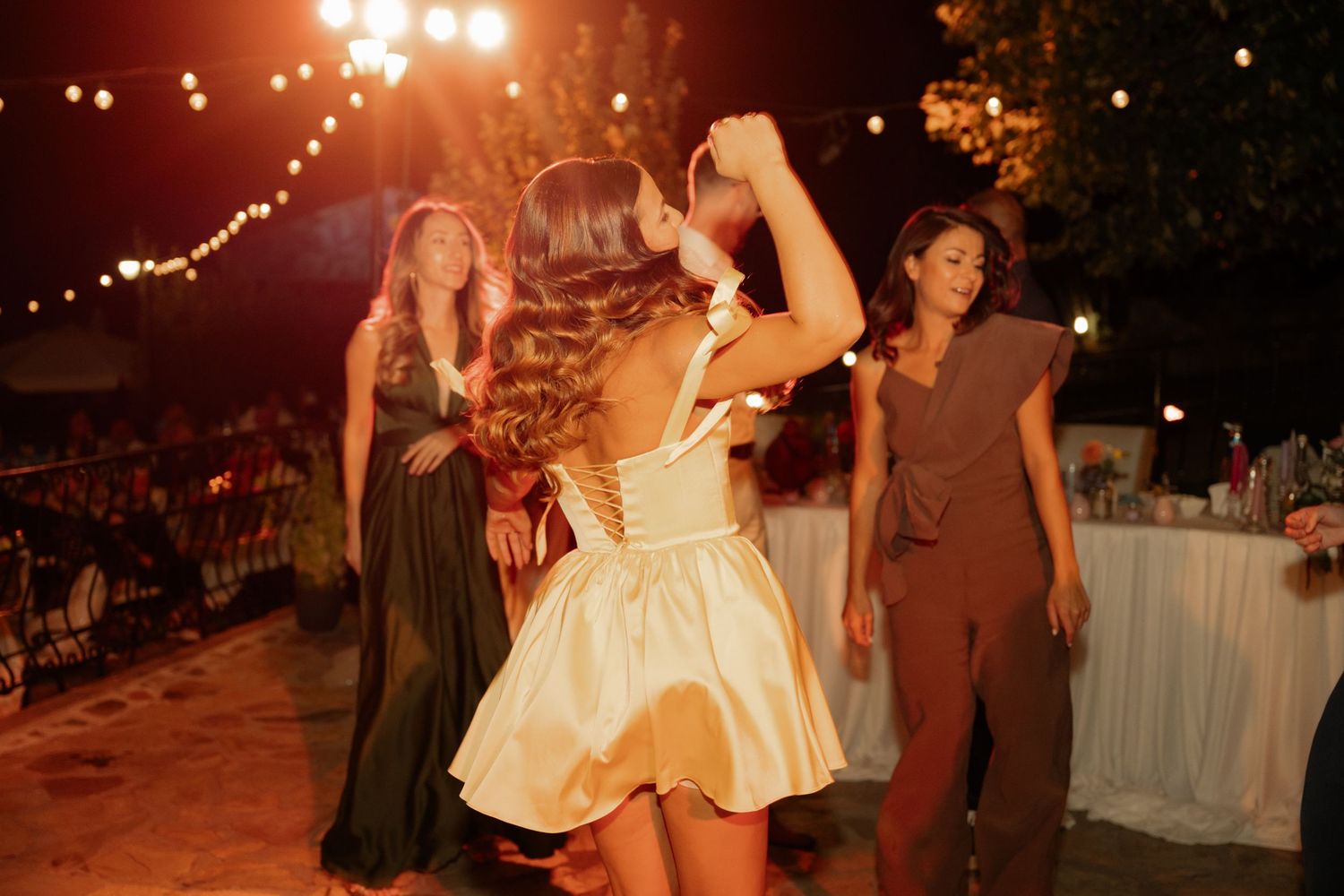 Wedding reception dance floor illuminated by warm string lights as guests celebrate at an outdoor evening party.