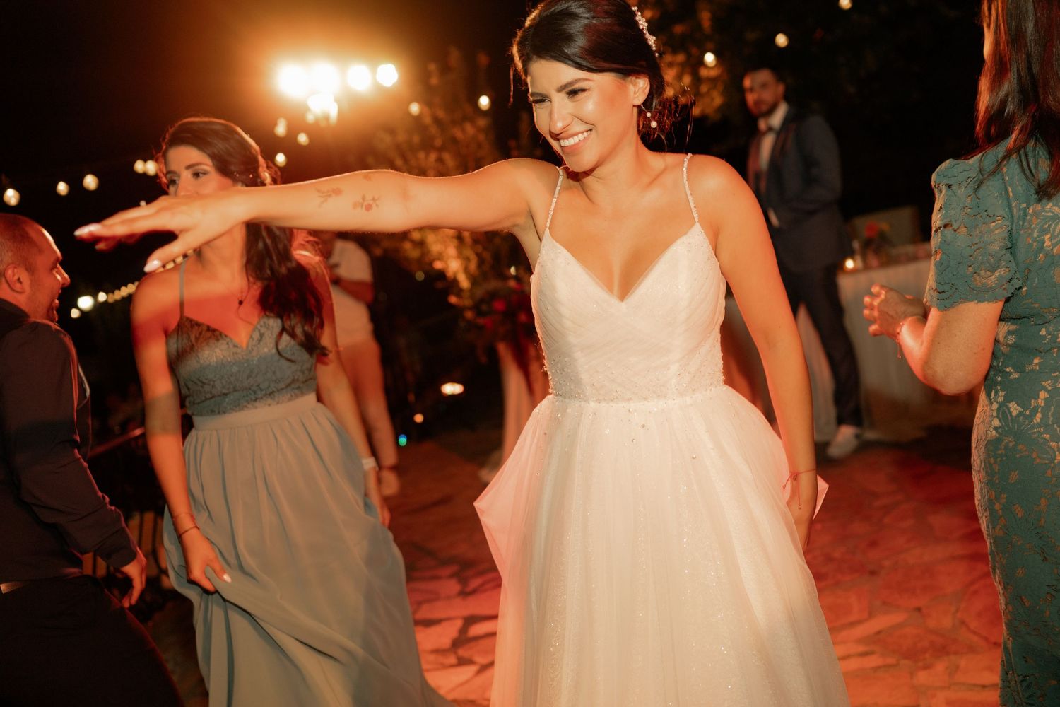 A couple dances together on an outdoor dance floor at night with warm lighting and other dancers in the background.