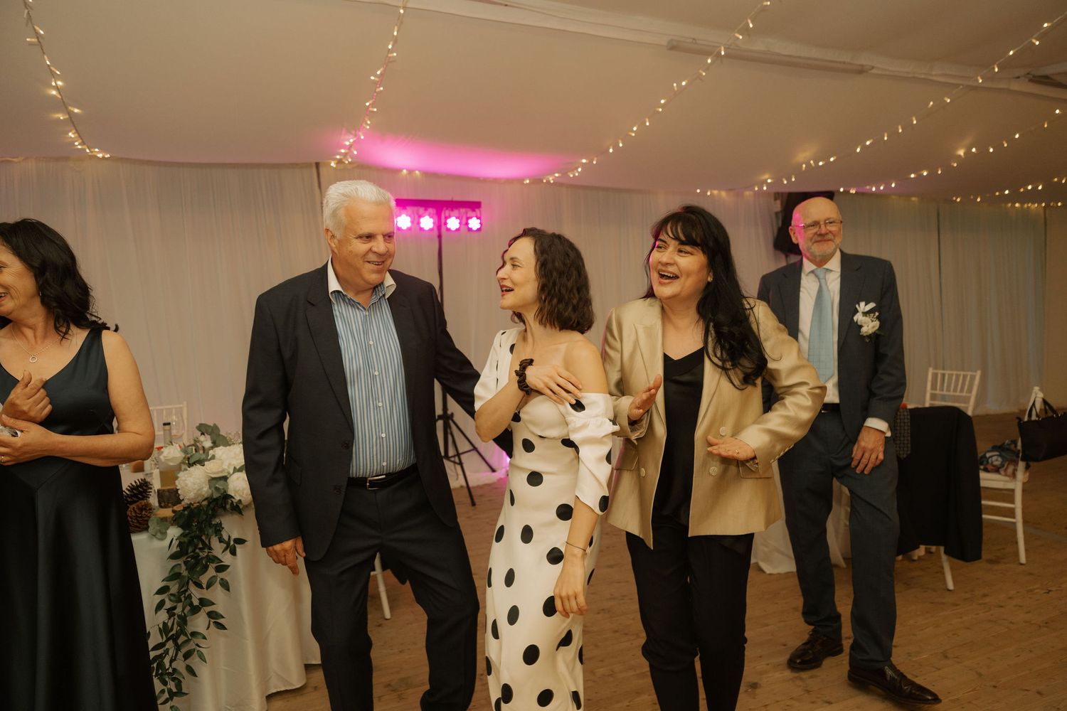Wedding guests laugh and dance together in a fairy light decorated reception venue.