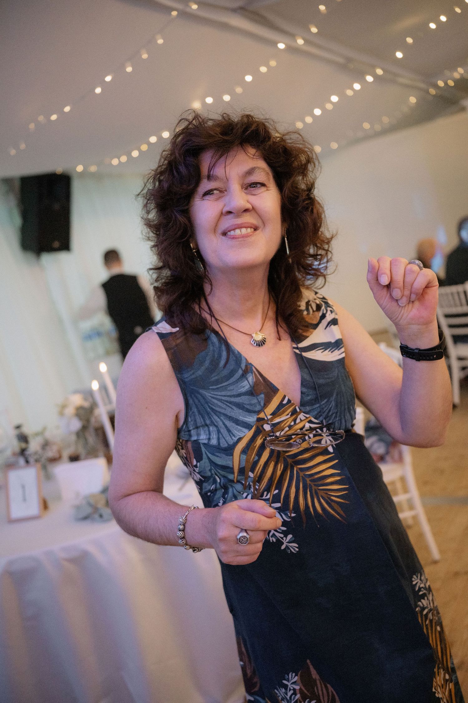 A woman in a floral dress smiles and dances at an elegant wedding reception with string lights.