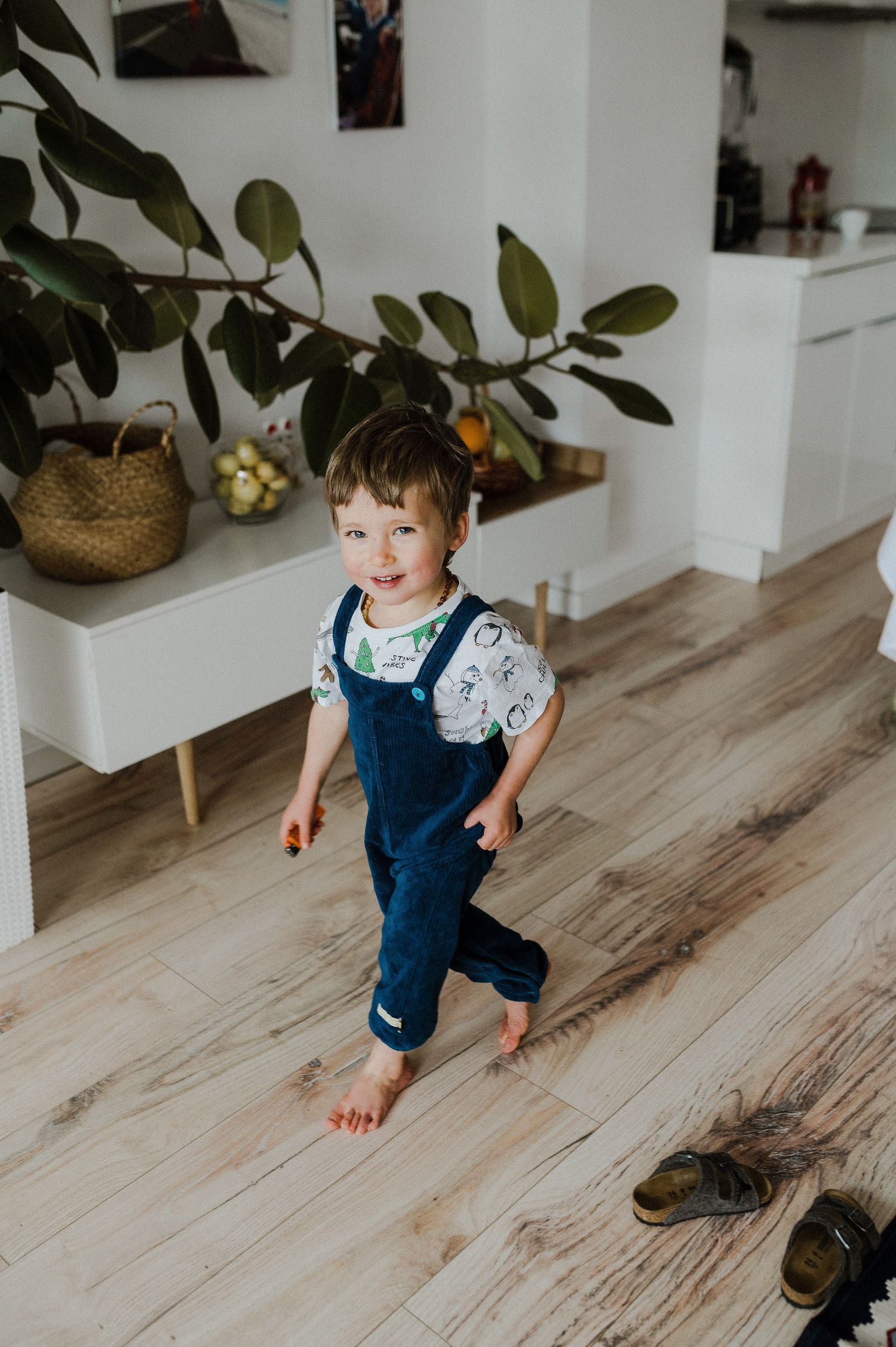 Small child running and playing on light wooden floors in a bright interior space with plants.