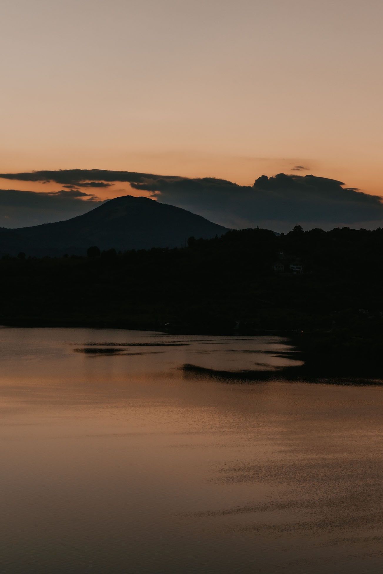 Serene lake landscape at dusk with mountains silhouetted against darkening sky.