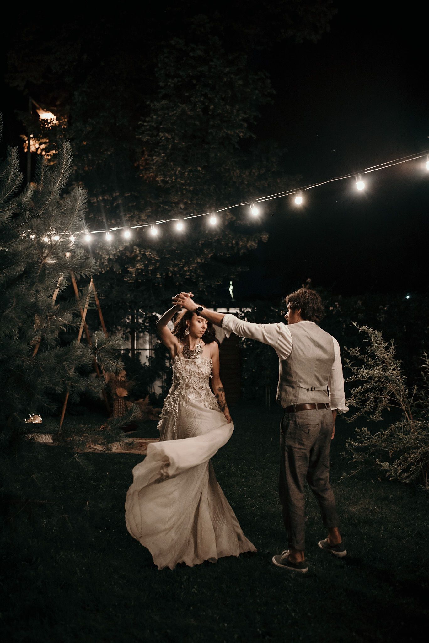A romantic nighttime dance scene under string lights in a garden setting with dreamy, moody lighting.