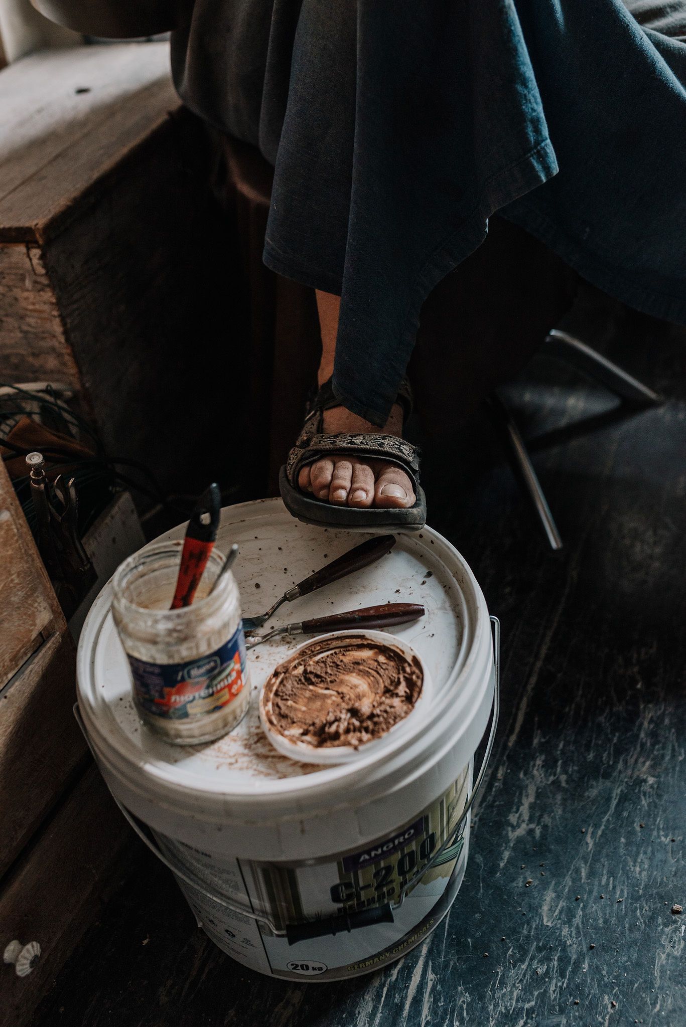 White bucket with chocolate spread being scooped out on a dark wooden floor.