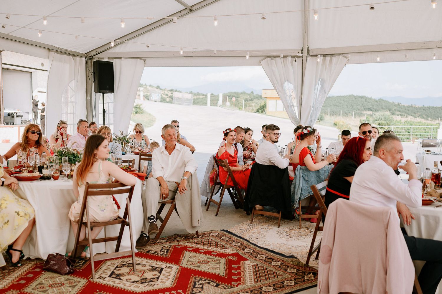 Large wedding tent interior with round tables and decorative lighting for an evening celebration.
