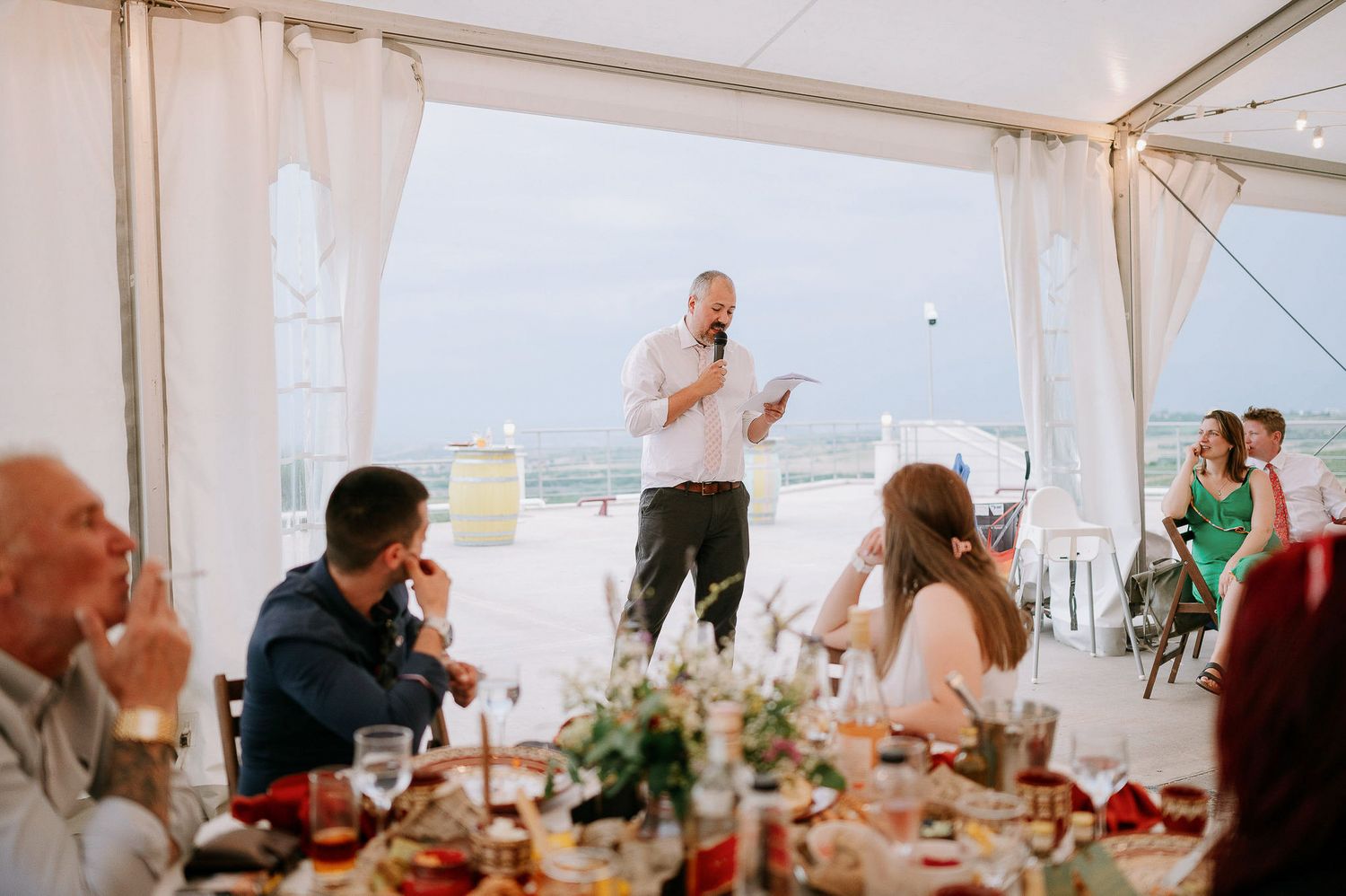Wedding celebration under white tent with guests seated at decorated round tables.