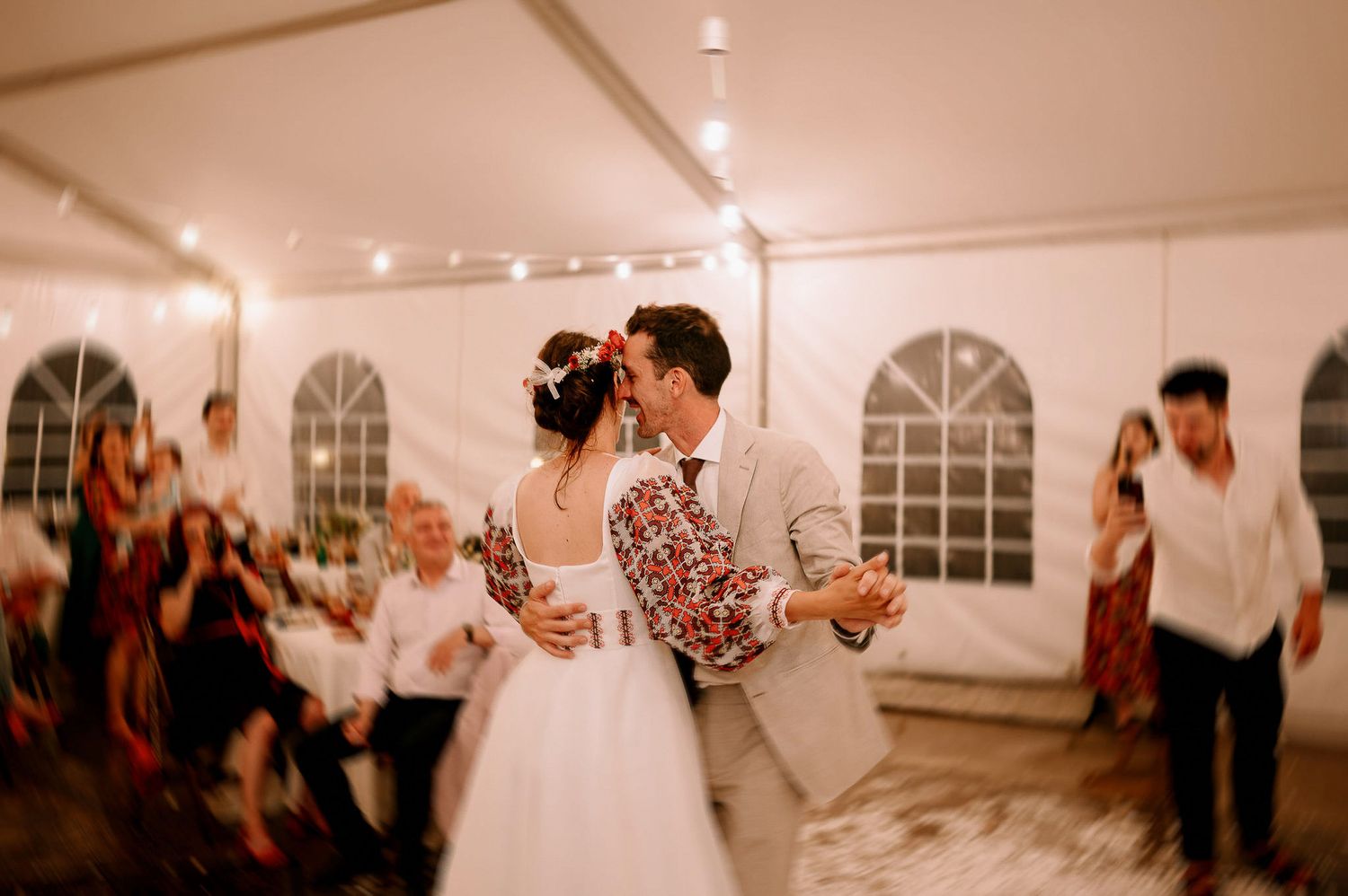 Guests dancing and mingling at an evening wedding reception in a decorated tent venue.
