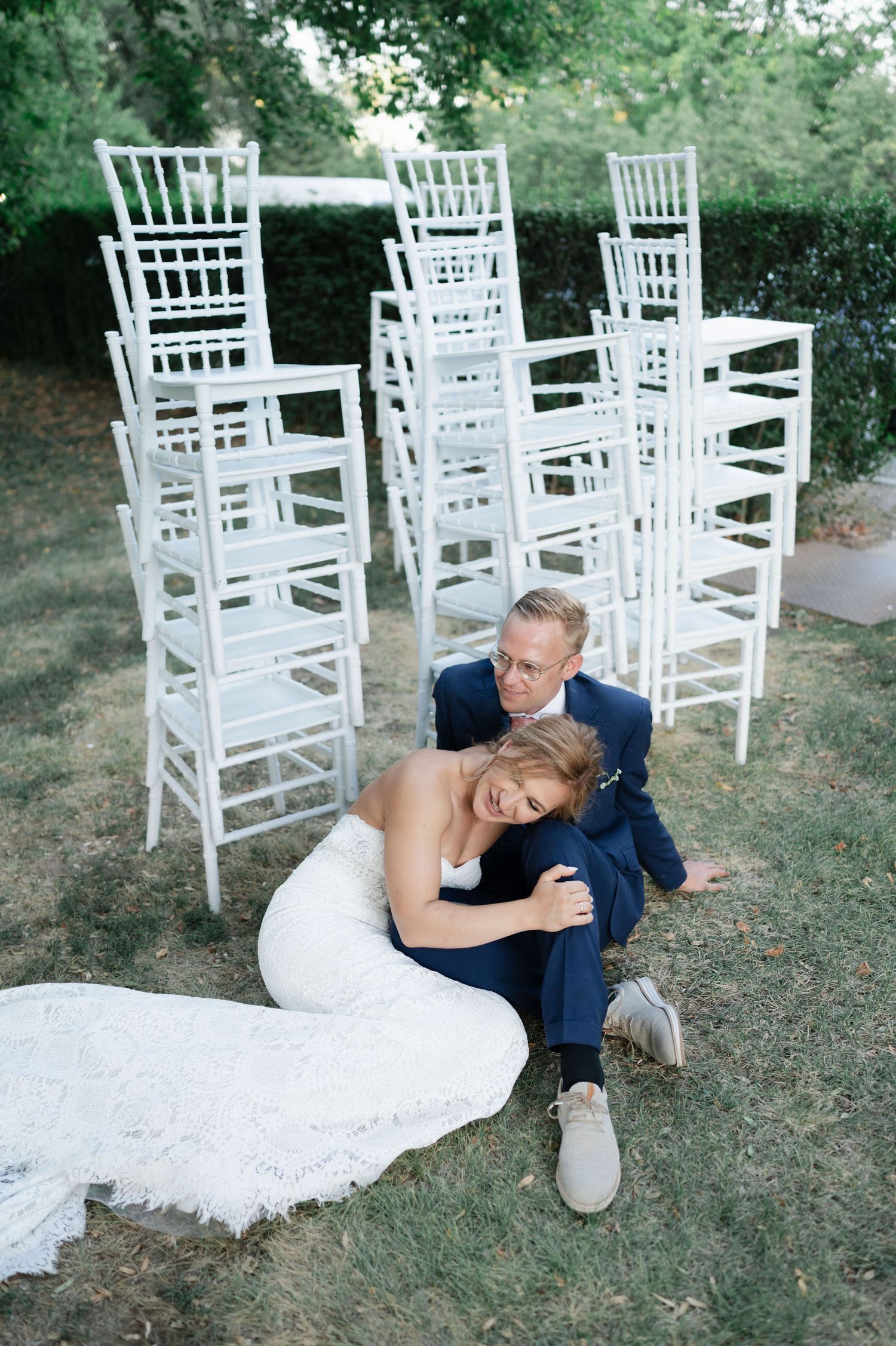 Candid wedding photo showing couple relaxing on lawn with white ceremony chairs in background.
