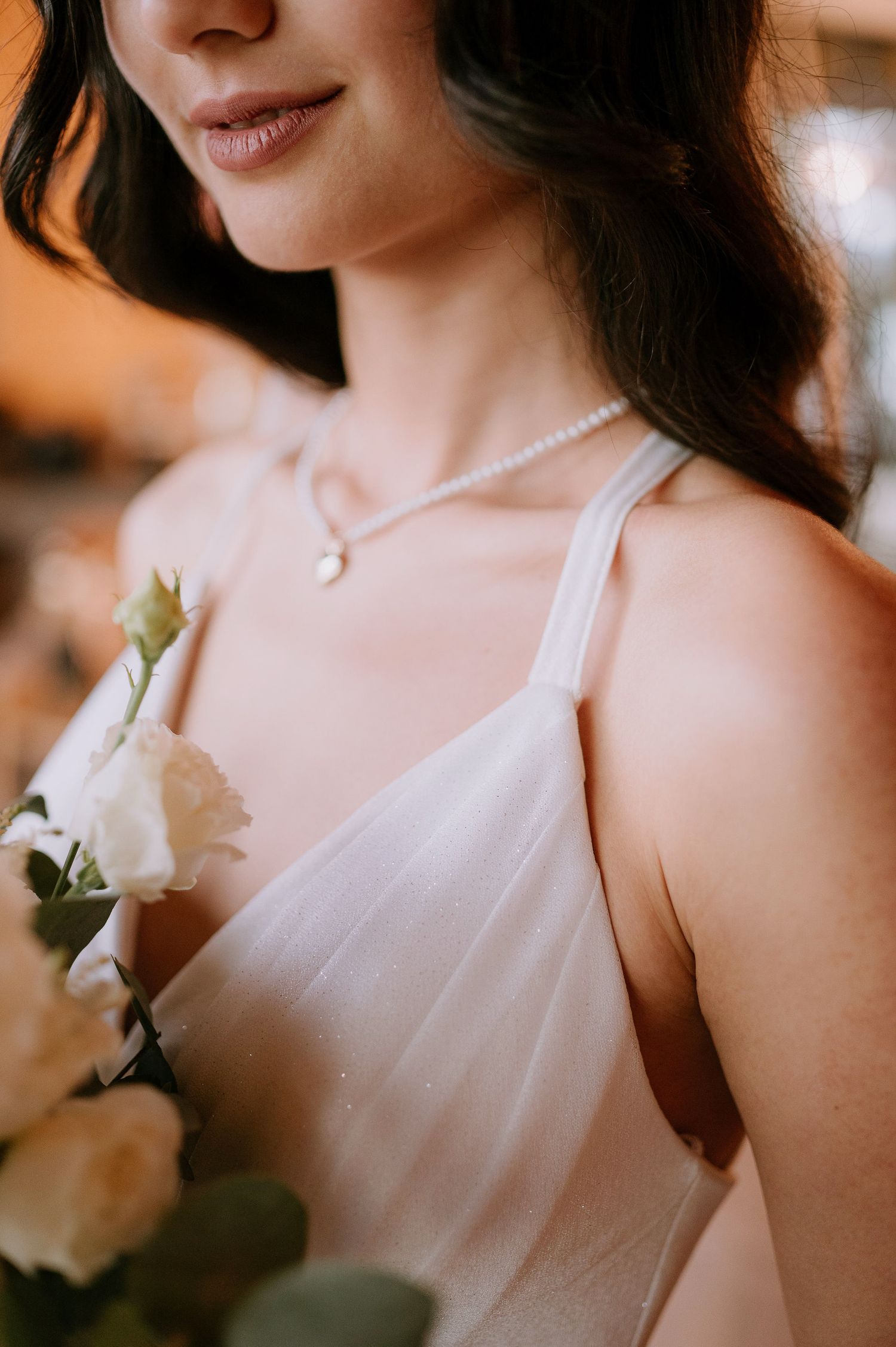 Close-up portrait showing white floral details and delicate pearl necklace against soft lighting.