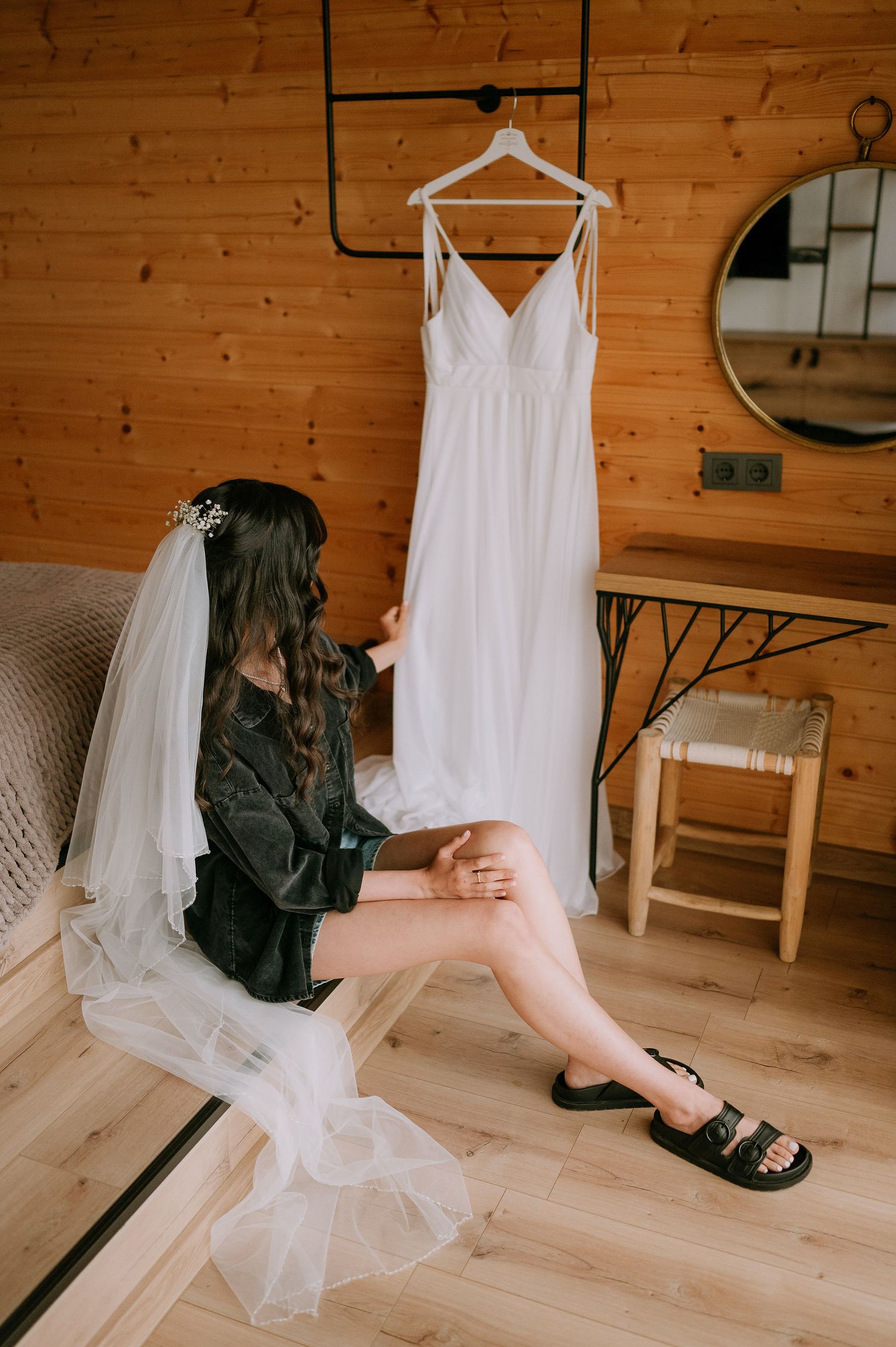 Interior scene with white wedding dress hanging while someone sits casually on wooden flooring.