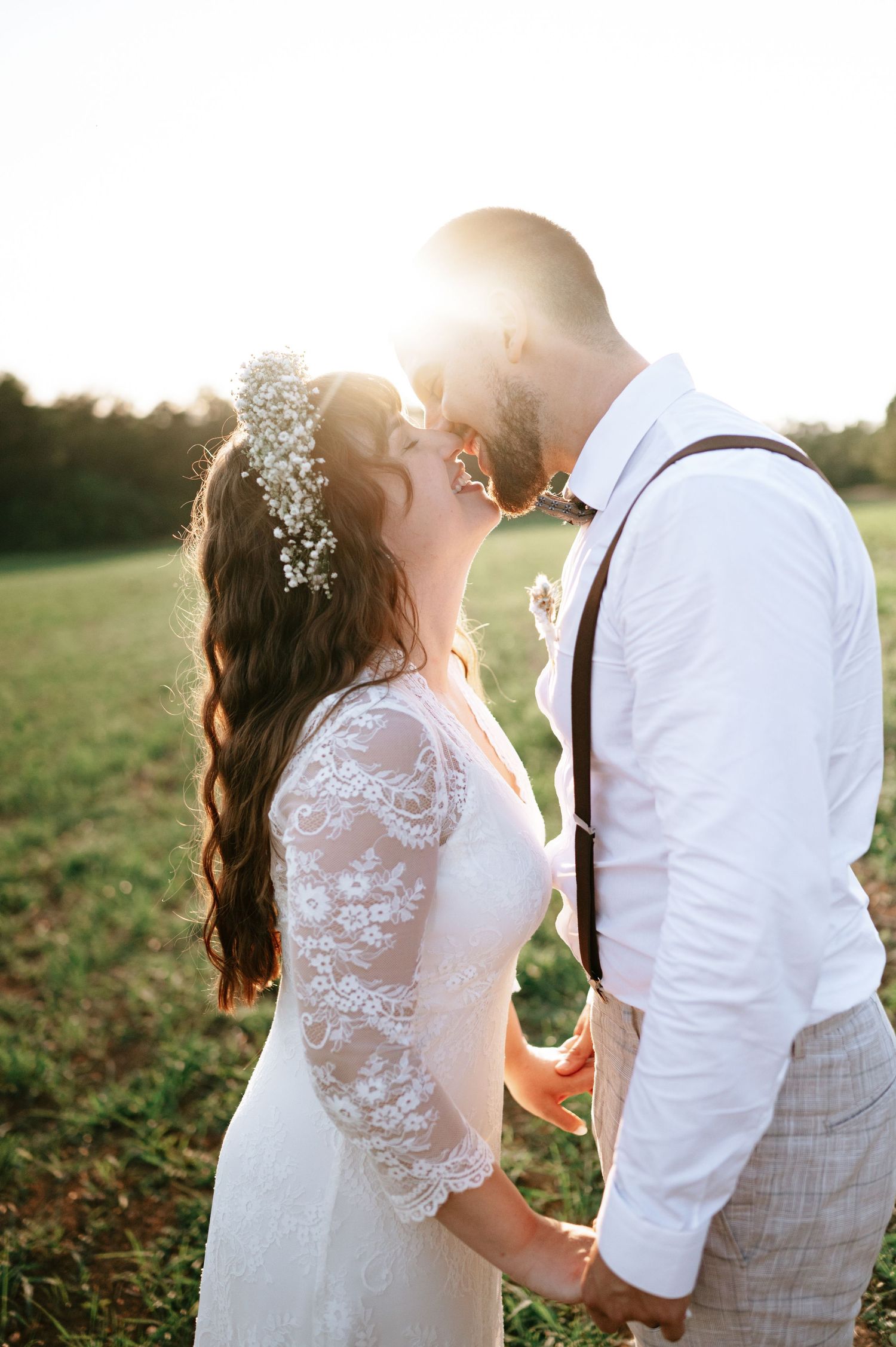 Bride in lace sleeves and groom share tender moment during sunset wedding photoshoot.