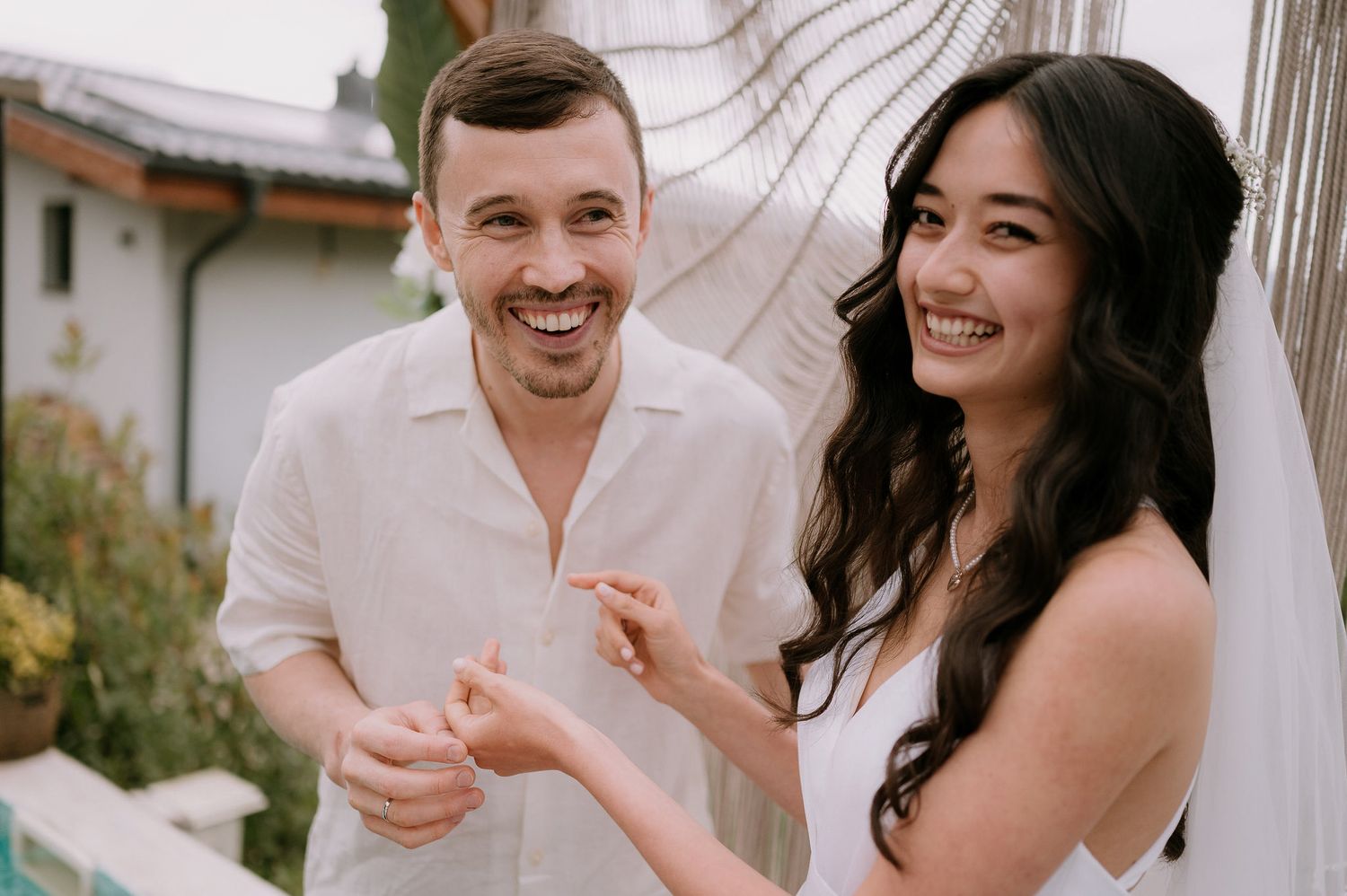 A couple laughing together while wearing matching white outfits at an outdoor venue.
