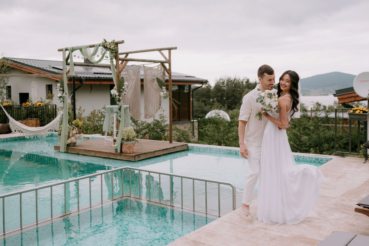 Wedding party gathered on a luxurious pool deck with mountain views in the background.