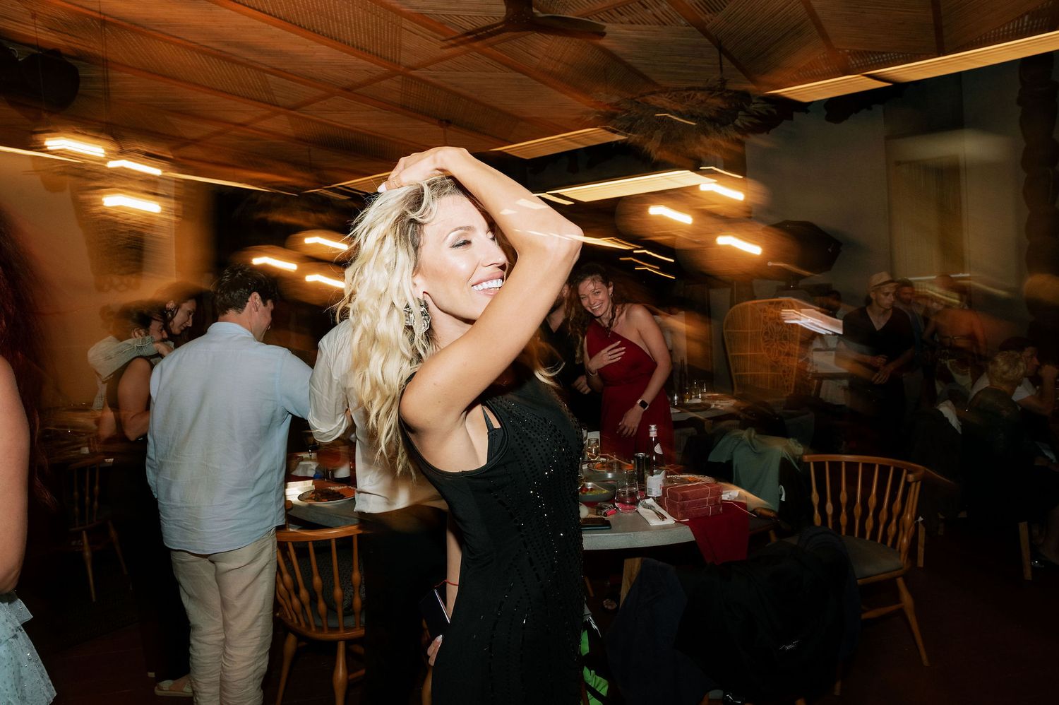 Crowd dancing and celebrating at an indoor event with wooden ceiling beams.